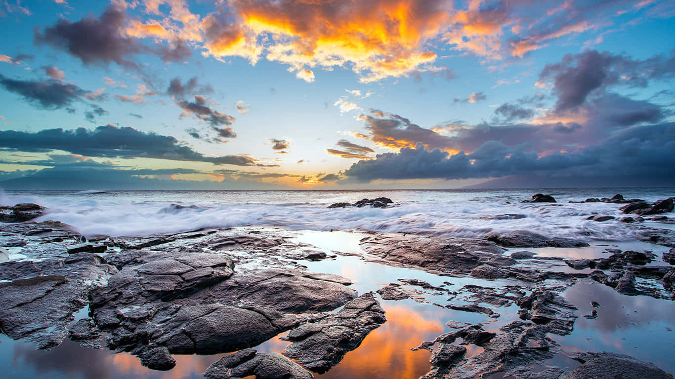 海浪輕拍海岸的寧靜場景 壁紙 — 夕陽將天空染成火熱的橙色和紫色，海浪拍打崎嶇的海岸岩石，映照出鮮豔的雲彩。