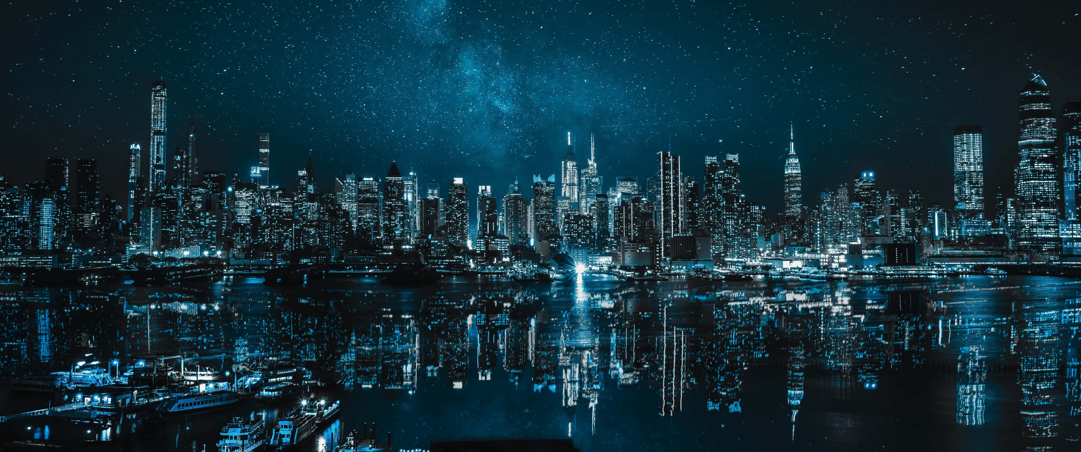 海港城市夜景 壁紙 — 令人驚嘆的夜景，摩天大樓在星空和銀河映照下閃爍，倒映在黑暗的水面上。