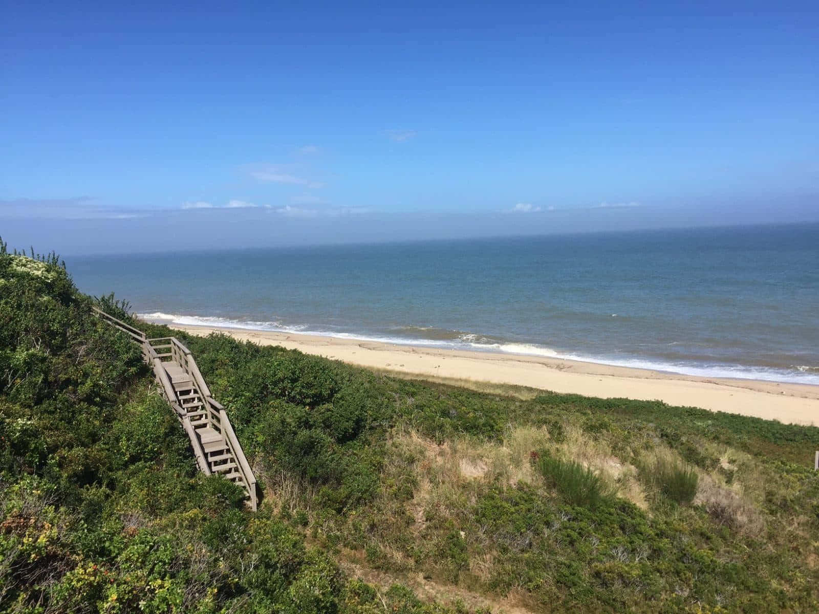 海濱小鎮日落美景 壁紙 — 一條木樓梯蜿蜒而下，穿過鬱鬱蔥蔥的綠色沙丘，通往晴朗藍天下寧靜的沙灘。