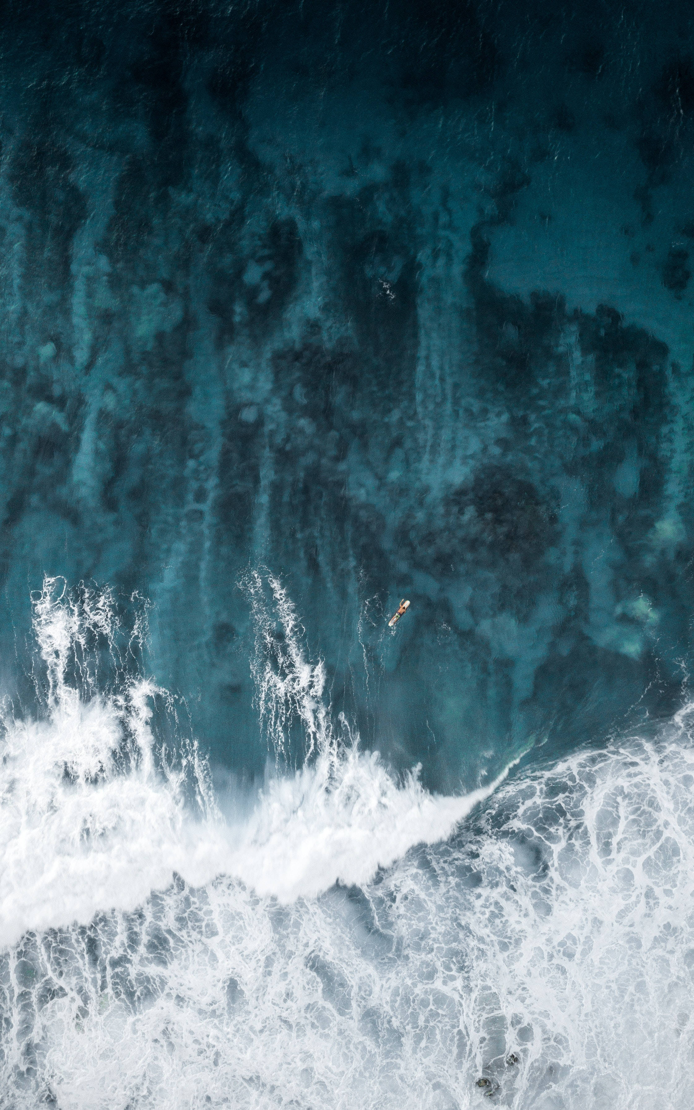 海濱衝浪 iPhone 解鎖畫面 壁紙 — 從空中俯瞰一名孤獨的衝浪者乘著帶有白色泡沫浪尖的巨大碧綠色海浪。