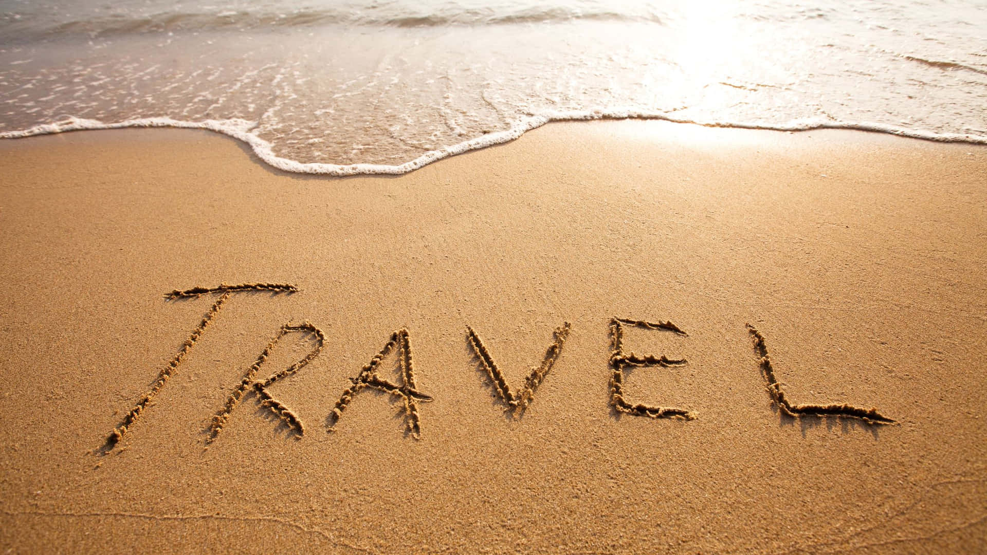 日落時分，海浪逼近，沙上寫住「travel」呢個字。