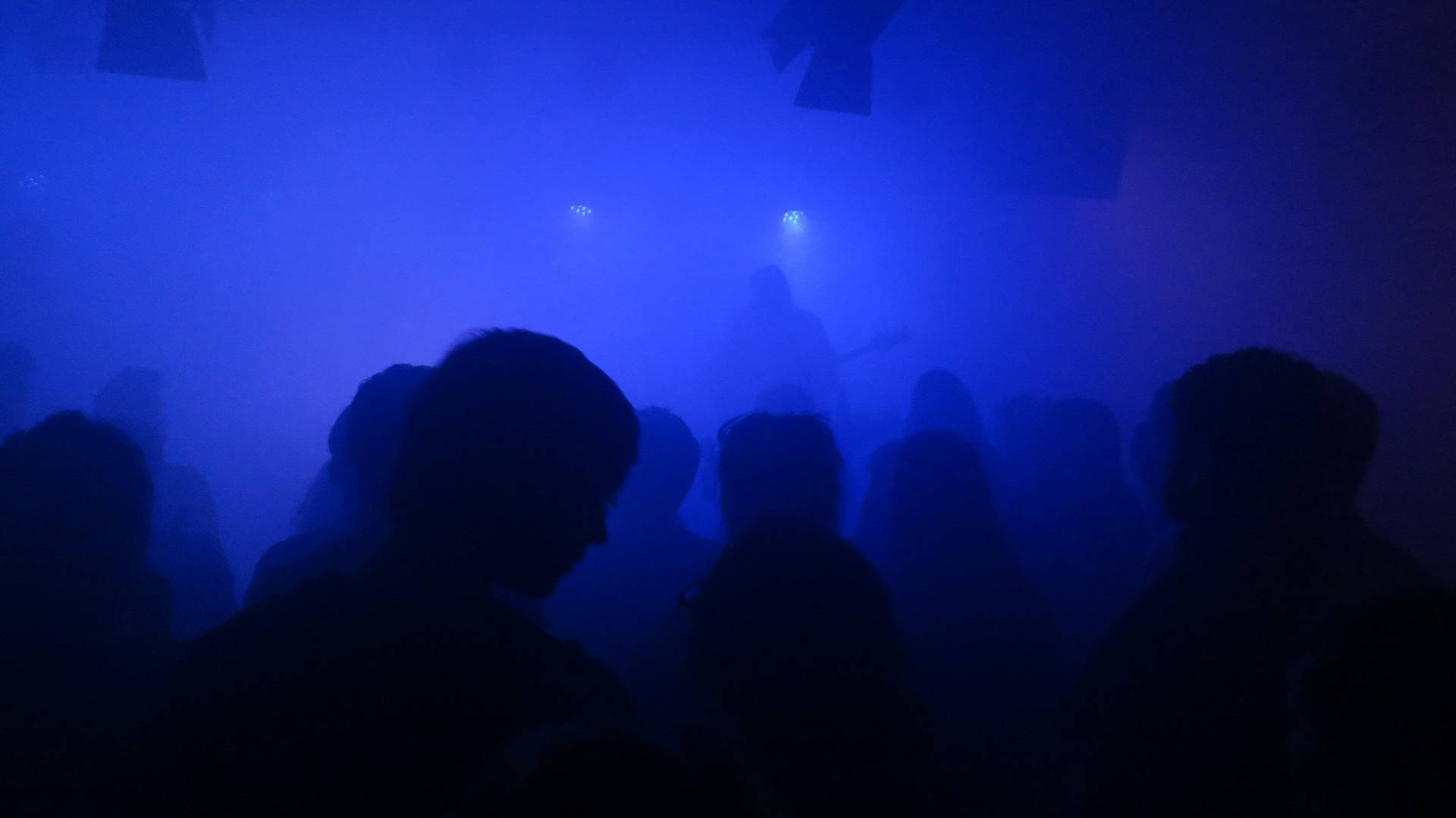 在藍色燈光煙霧彌漫的夜店中，人群的剪影。