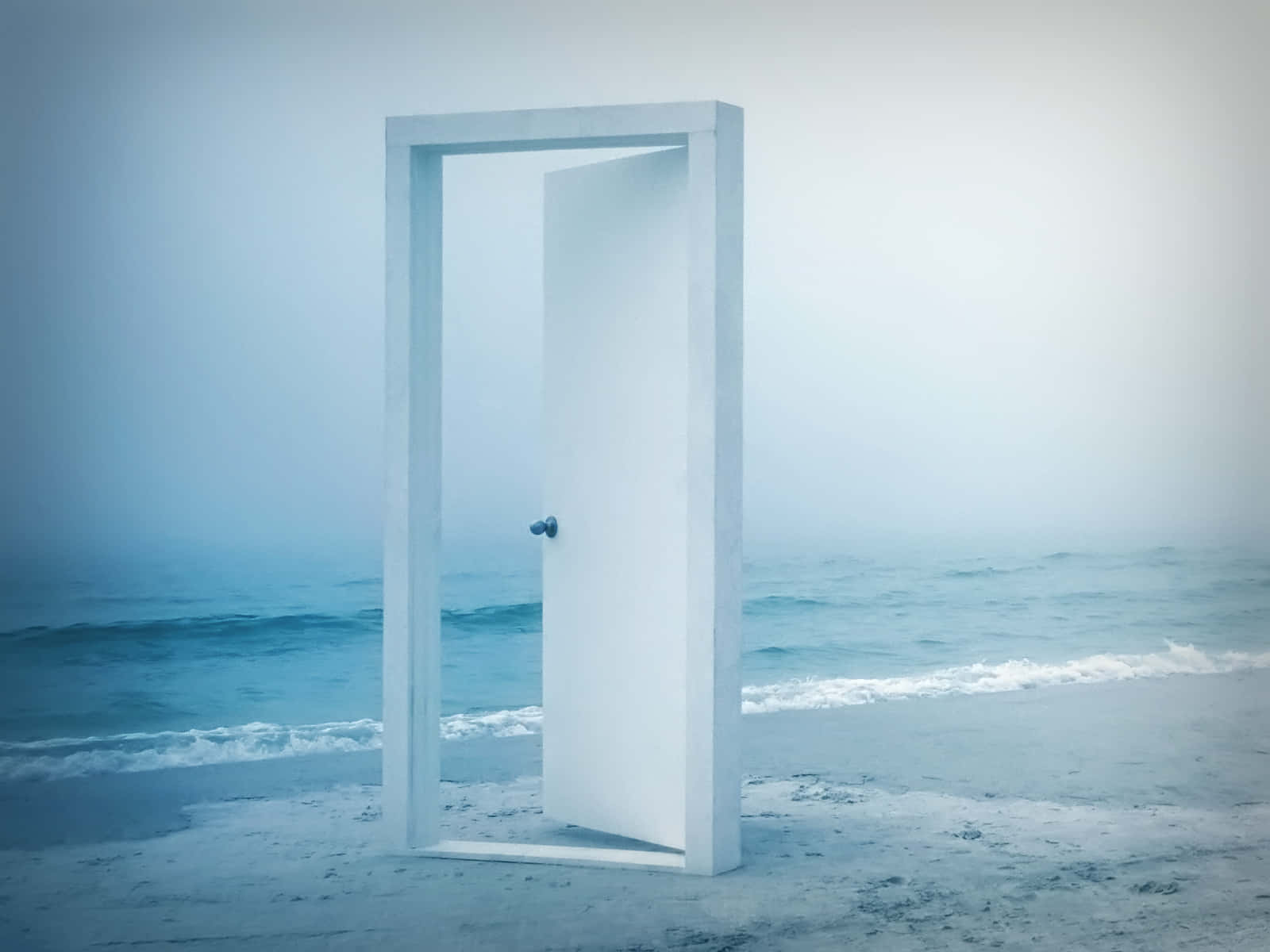 一扇白色門打開在霧濛濛的海灘上，面向海洋。