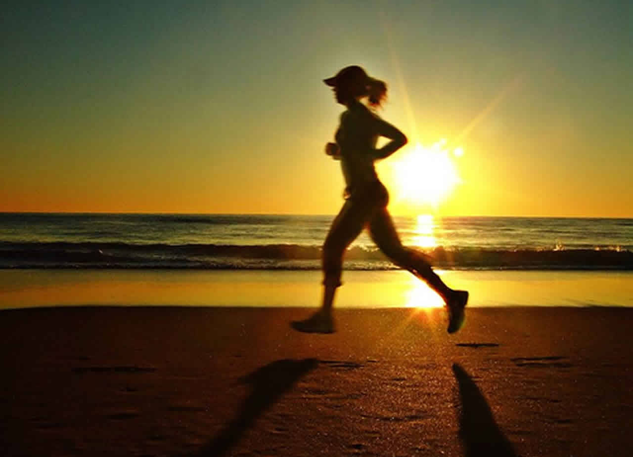 海灘上跑步復健的女性剪影 壁紙 — 日落時分，一名跑步者在海灘上慢跑的剪影，身後拖著長長的影子。