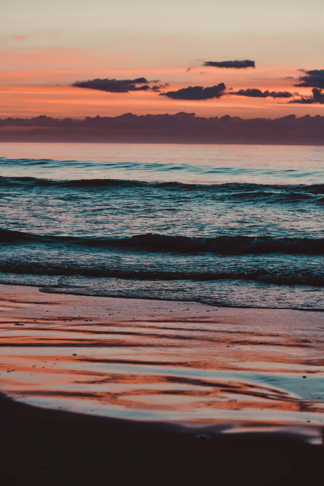 夕陽映照海洋，海浪沖刷濕沙，反射出溫暖的色彩。