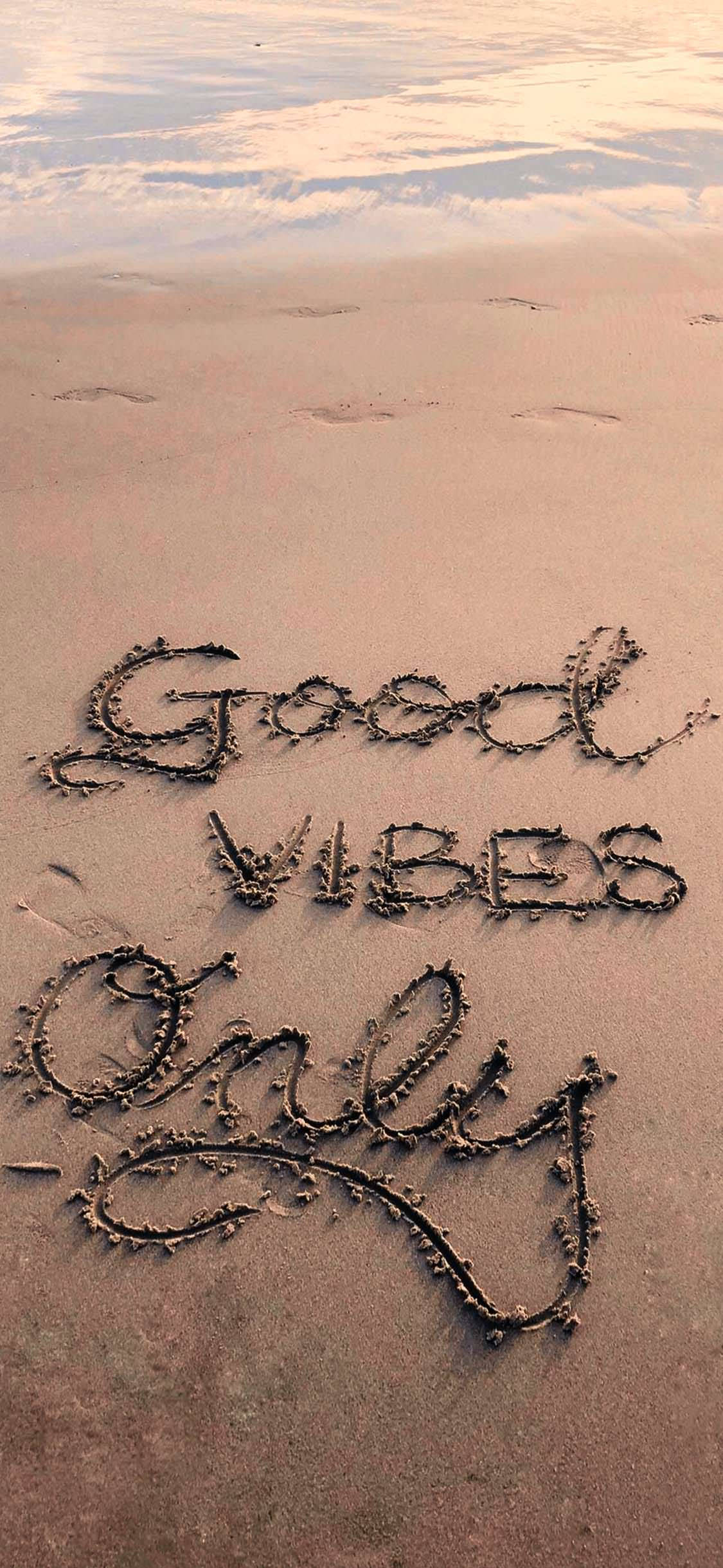 海灘好氣氛 壁紙 — 「Good Vibes Only」呢句短語以草書寫喺濕沙上，背景有柔和嘅海浪同天空倒影。