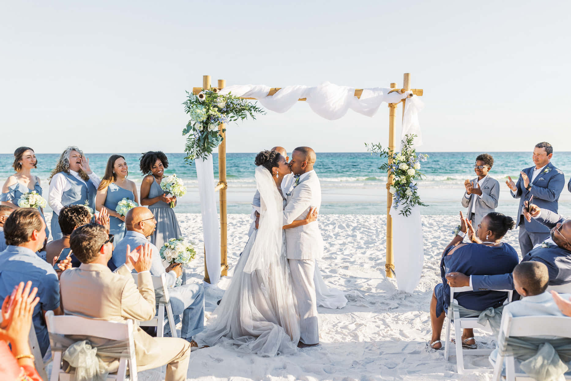 一對新人在海灘婚禮上接吻，賓客鼓掌。