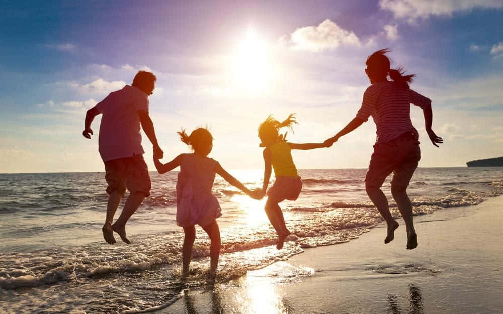 海灘家庭共聚營火，情誼無價 壁紙 — 一家四口在陽光明媚的海灘上歡樂地齊齊跳躍，金色海浪在他們腳下拍打。