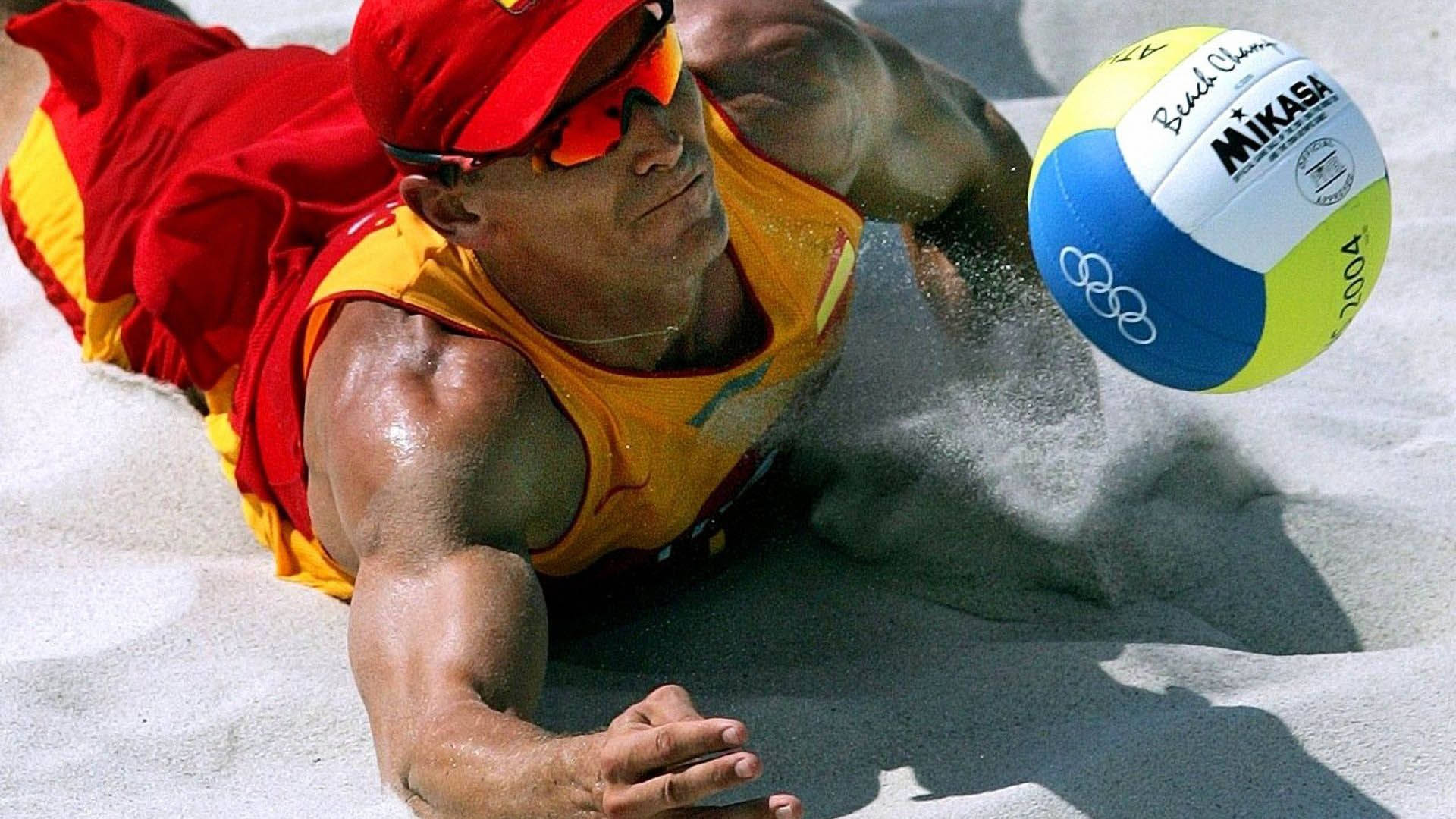 海灘排球選手哈維爾·博斯馬救球 壁紙 — 一名肌肉發達的沙灘排球運動員，身穿紅黃色裝備，在烈日下潛入沙中扣殺 Mikasa 排球。