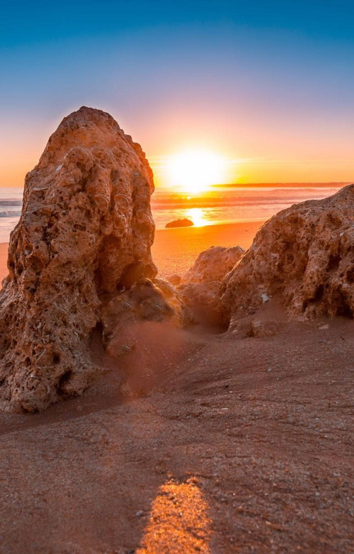 岩石海灘上的夕陽，沙灘和波浪上溫暖的金色光芒