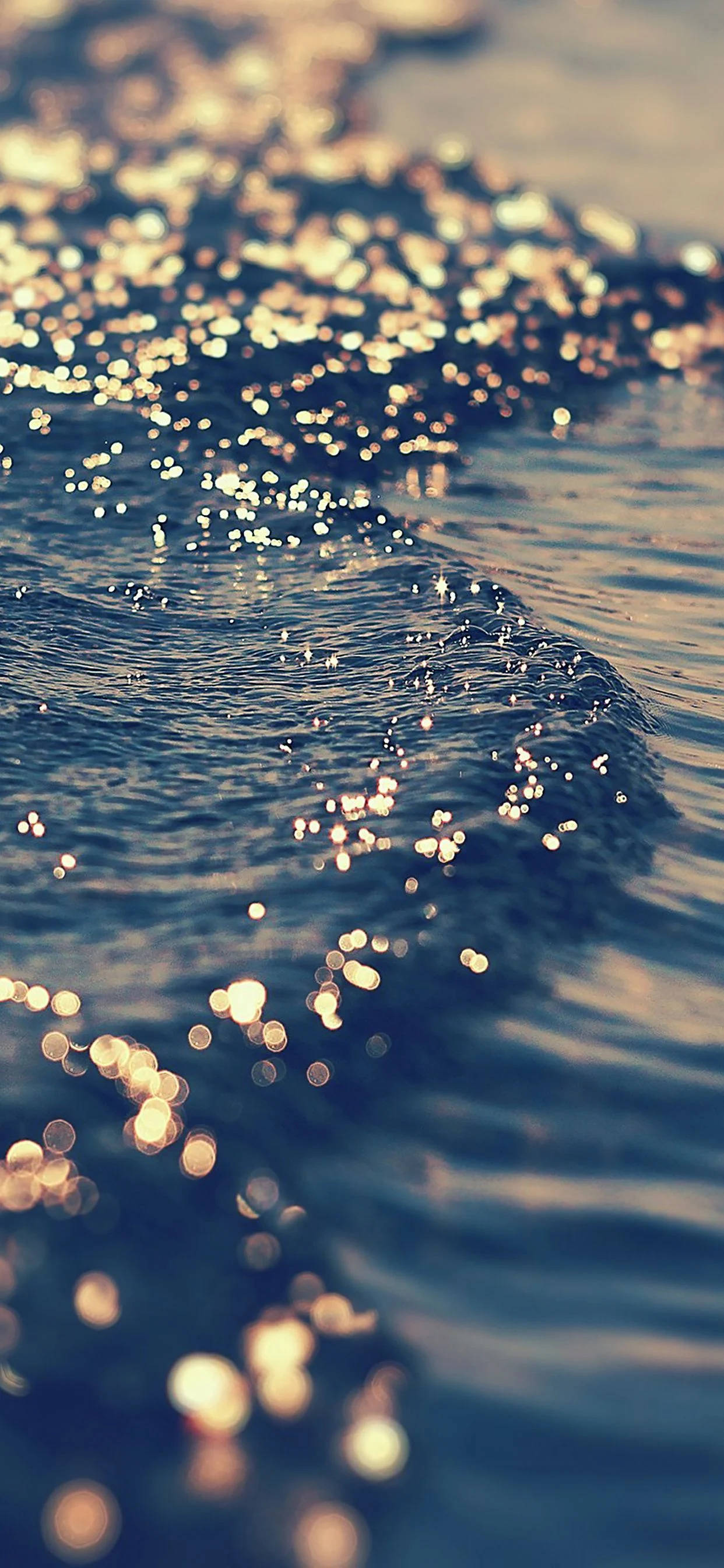 海灘日落美景 壁紙 — 陽光在漣漪的海浪上舞動，在深藍色的海水中營造出閃爍的金色散景效果。