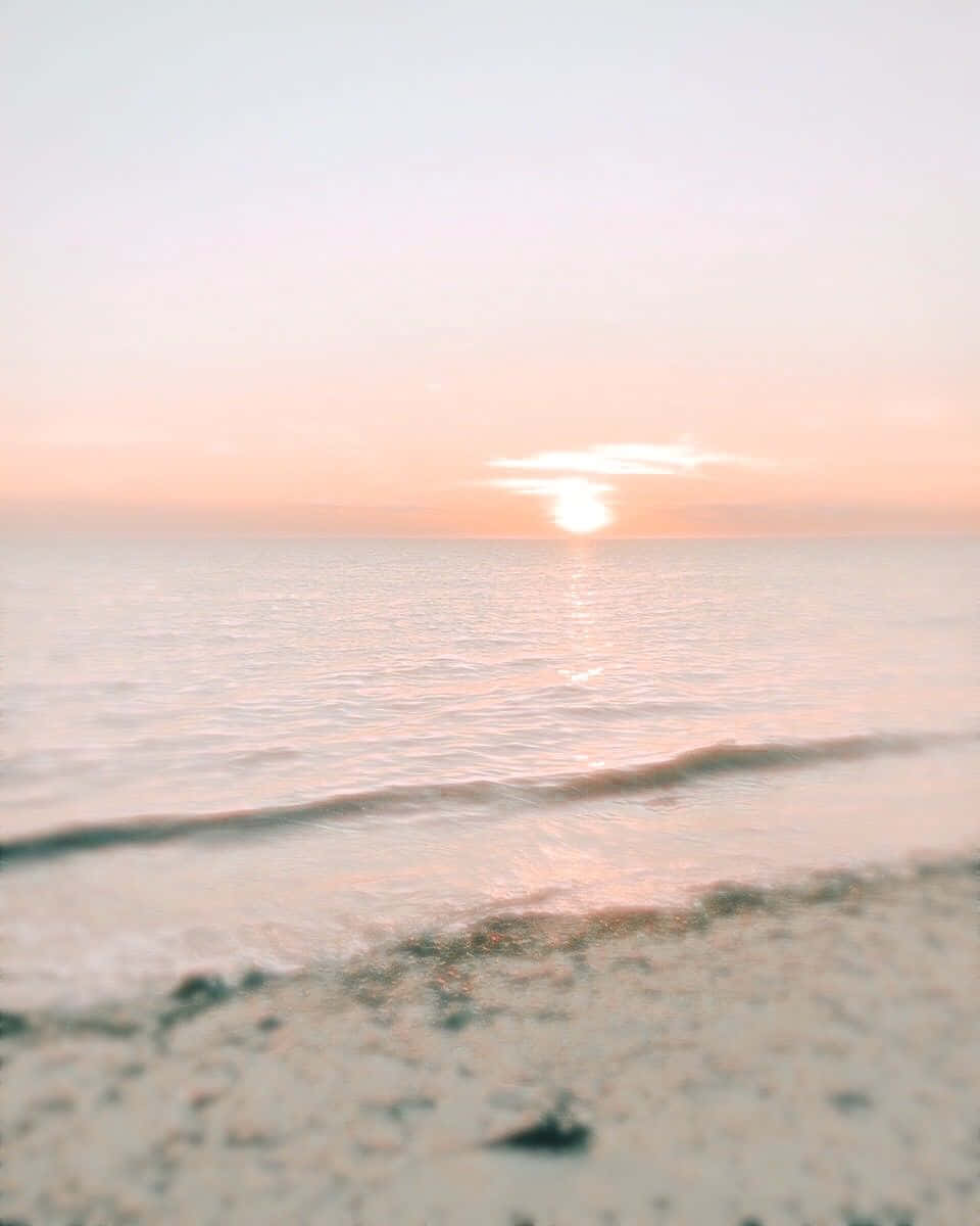 海灘日落風景圖 壁紙 — 柔和的粉紅色日落照耀著平靜的海水與沙灘交匯處，呈現輕柔的模糊效果。