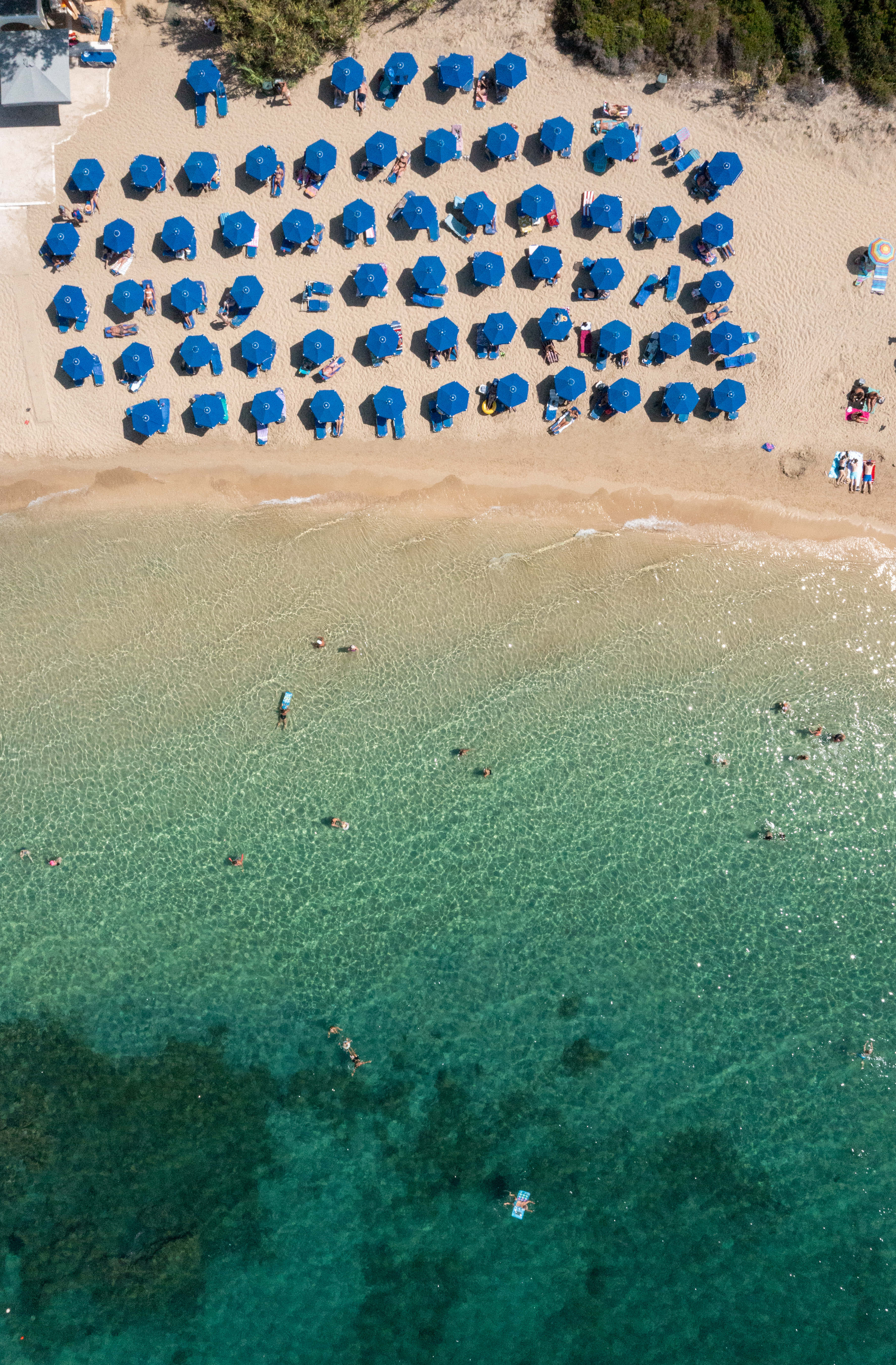 Mediterranean Beach 桌布 壁紙 — 海灘的鳥瞰圖，排列著藍色遮陽傘，人們在碧綠的海水中游泳。