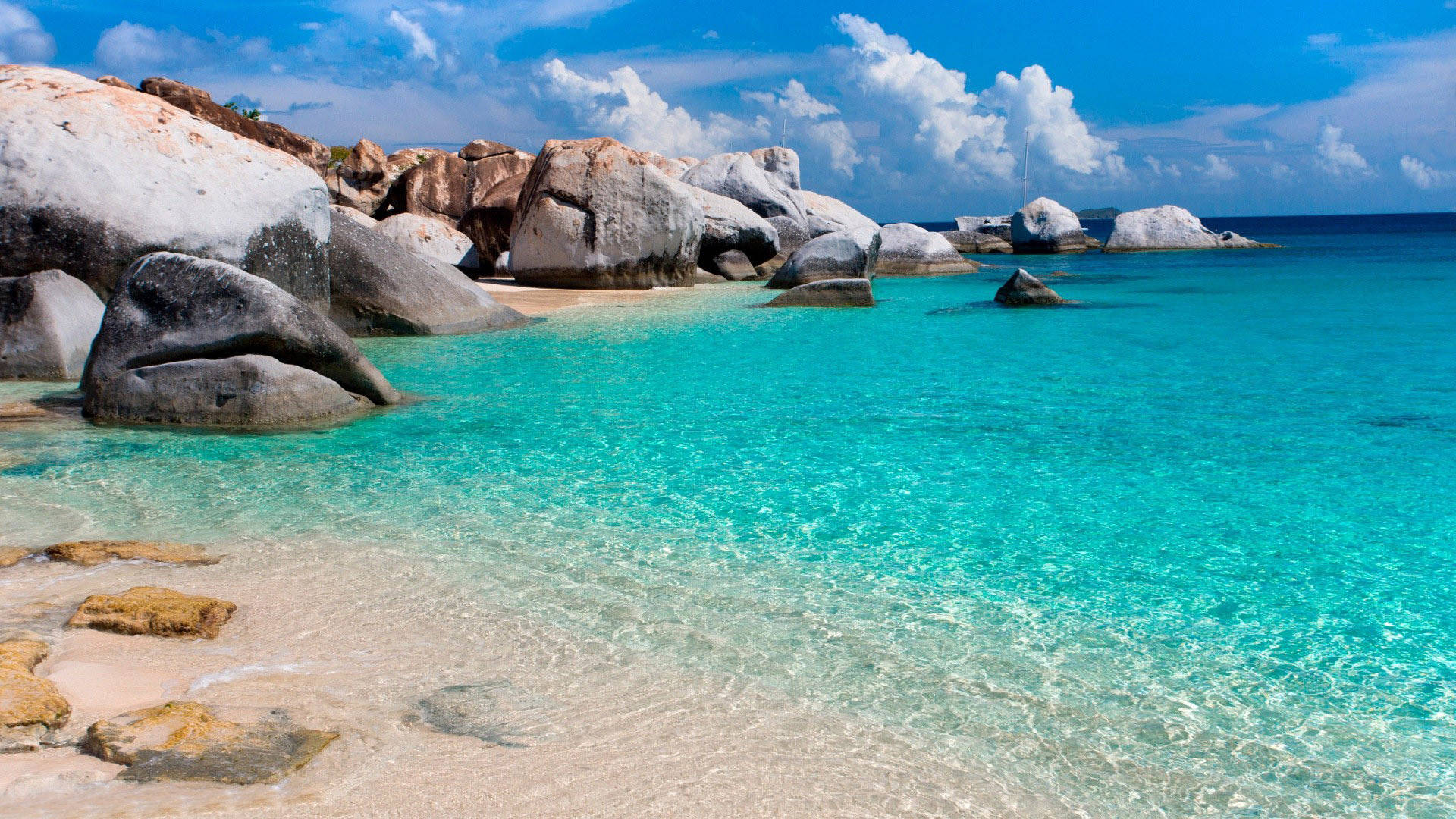 海灘自然風景 壁紙 — 清澈的碧綠海水拍打著白色沙灘，沙灘周圍是巨大的風化岩石，上方是明亮的藍天和蓬鬆的白雲。