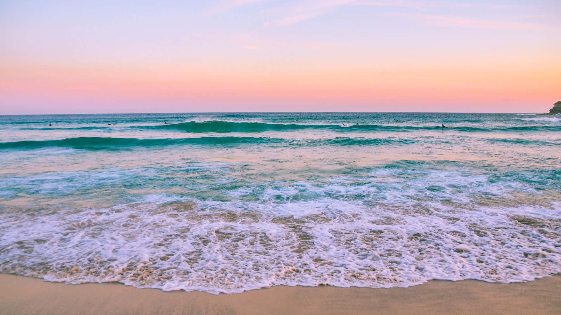 海灘風景 潮汐夕照 壁紙 — 夕陽將天空染成柔和的粉紅色和橙色，溫柔的海浪拍打著沙灘，遠處有衝浪者。