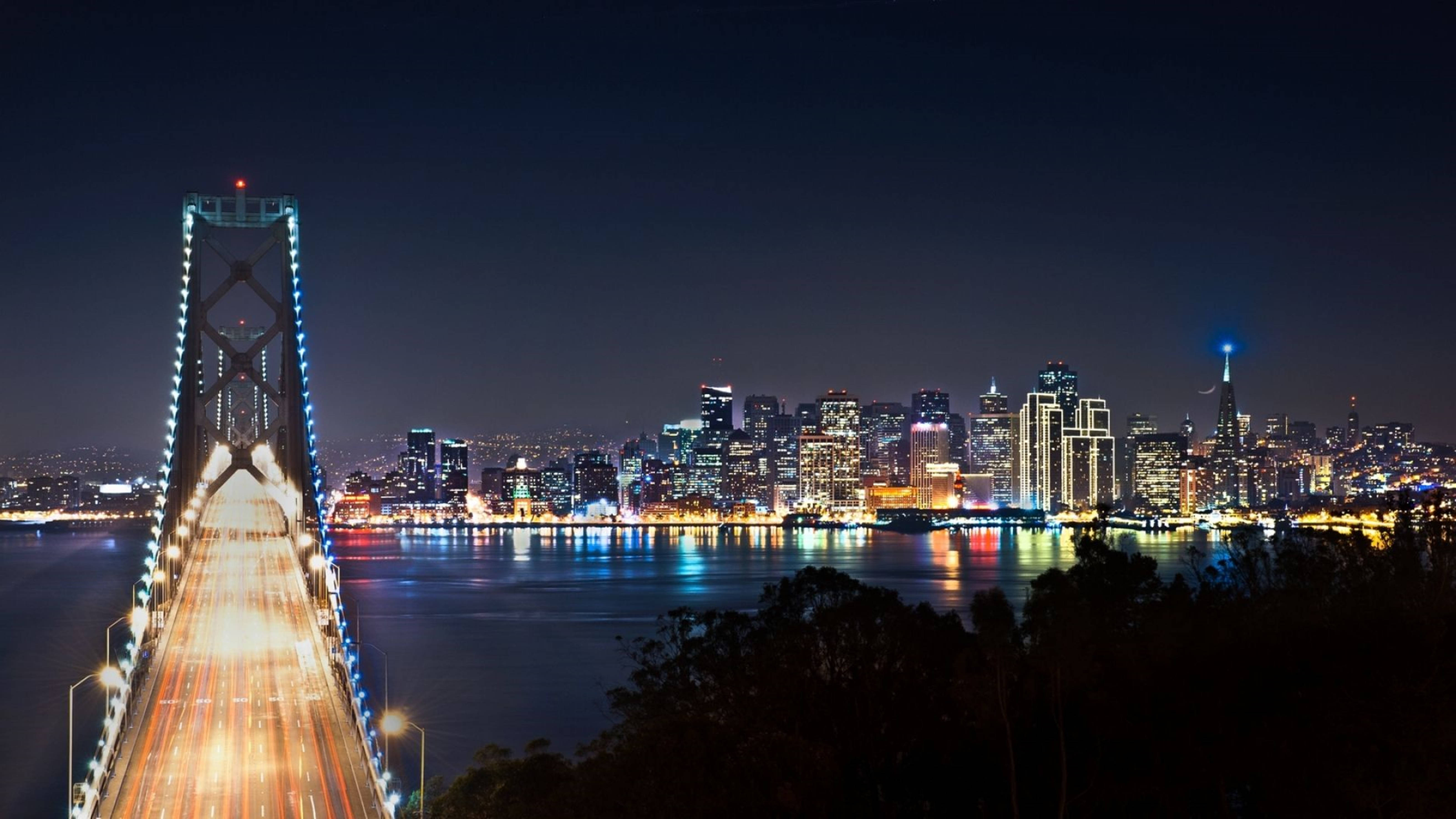 風景動圖 桌布 壁紙 — 海灣大橋和舊金山天際線的迷人夜景，璀璨的城市燈光倒映在水面上。