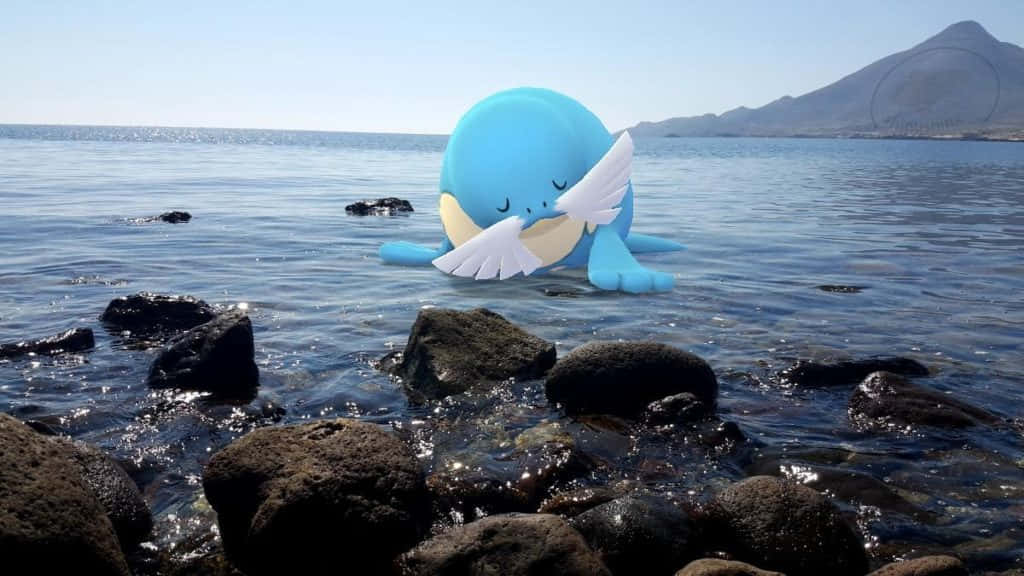 海獅在野外 壁紙 — 一隻有白色翅膀的藍色卡通鯨魚在晴朗的天空下，在黑暗的火山岩附近平靜的海水中安詳地漂浮。