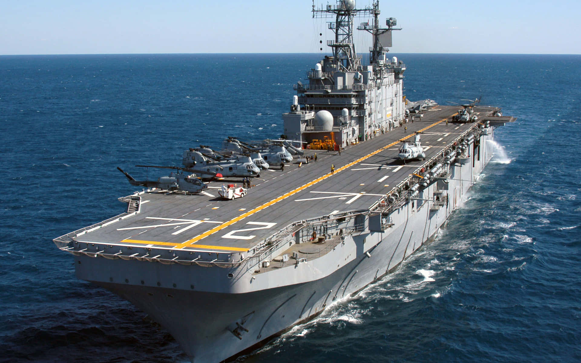 海軍人員執行巡邏任務 壁紙 — 一艘大型灰色航空母艦在深藍色海洋中航行，飛行甲板上停有直升機。