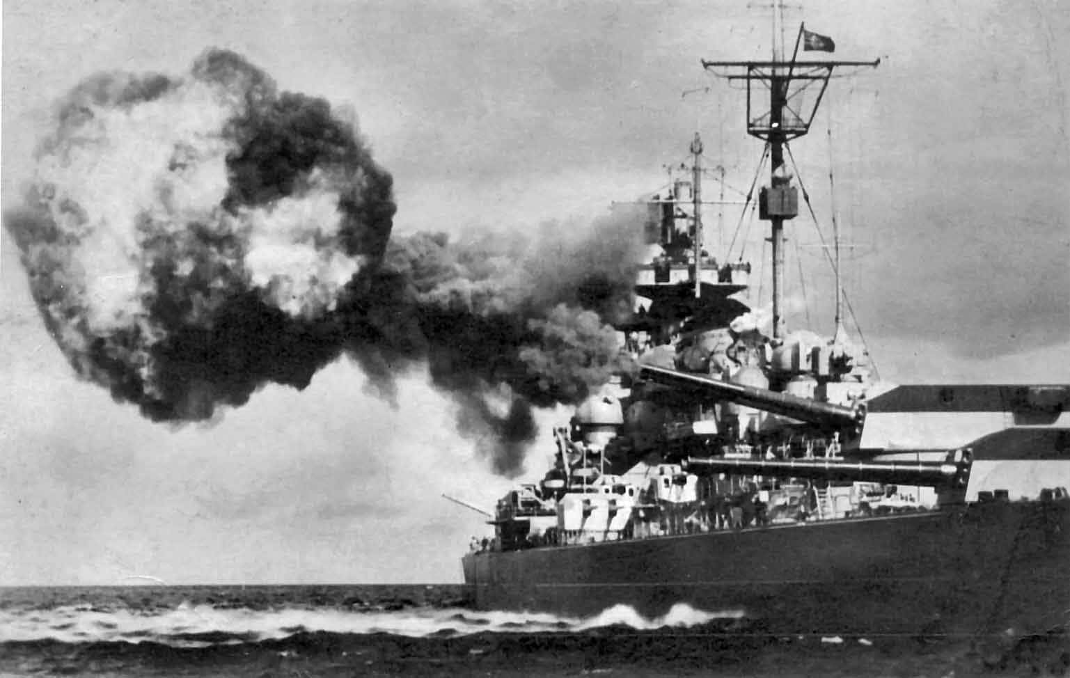 海軍戰艦駛過碧海 壁紙 — 一艘戰艦發射主炮，在波濤洶湧的海面上切開，向陰沉的天空噴出巨大的煙霧。