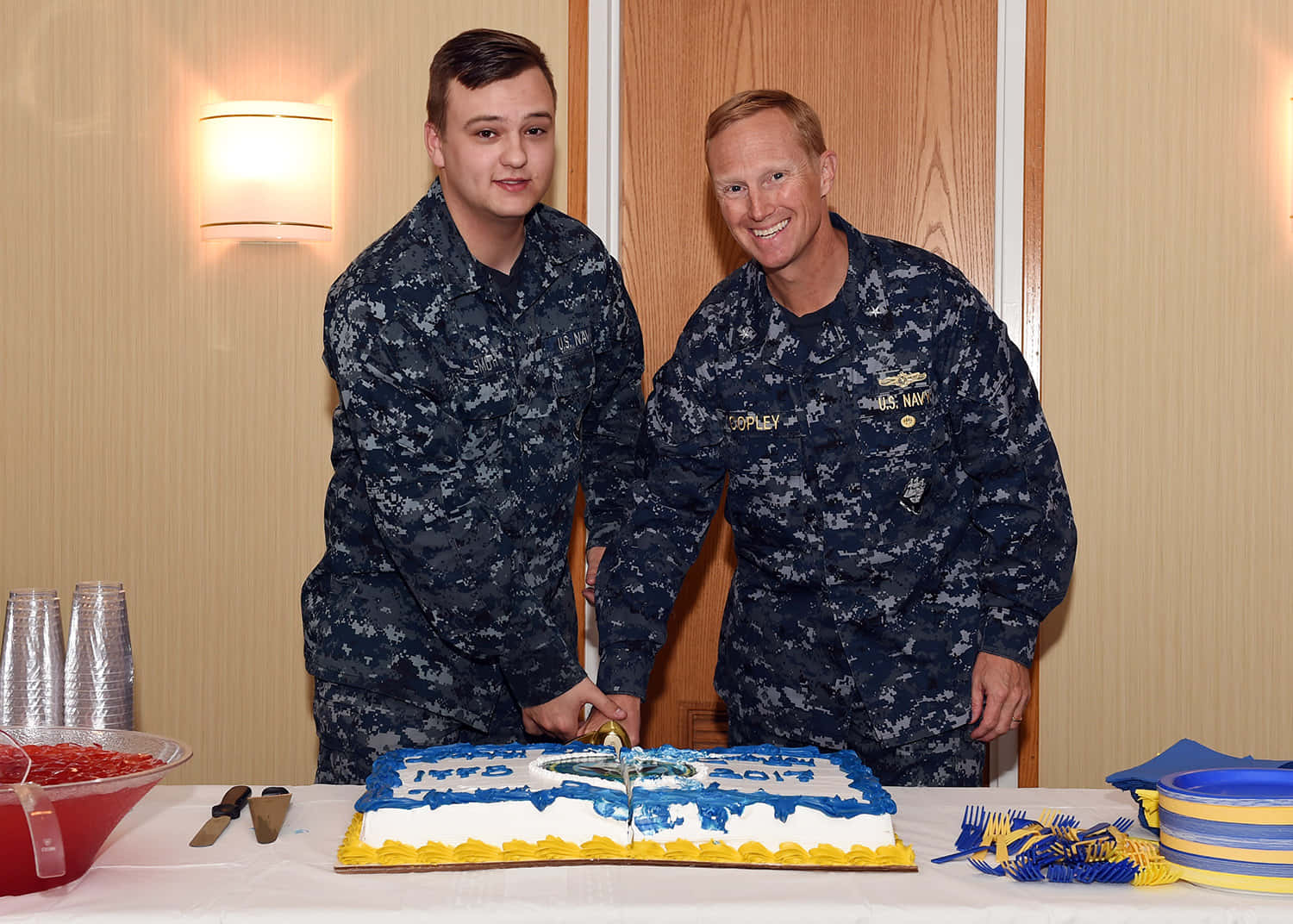 海軍生日慶祝切蛋糕 壁紙 — 兩位面帶微笑的海軍軍官身穿迷彩服，在慶祝活動中一起切一個藍黃相間的蛋糕。