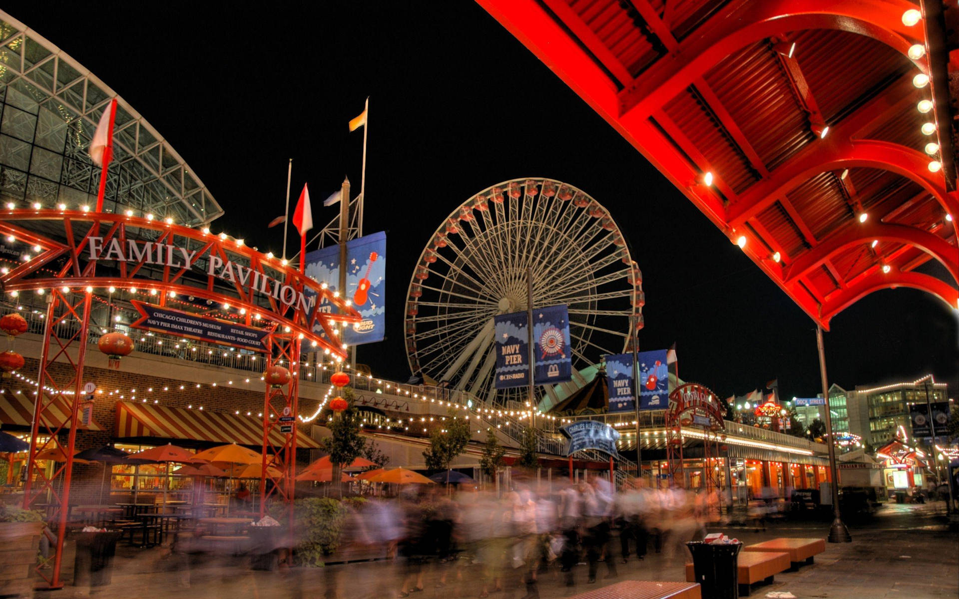 夜間遊樂園，有摩天輪和紅色天篷，在燈串下。