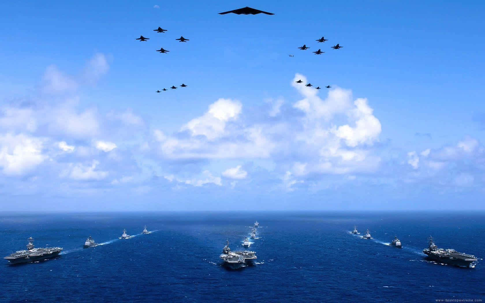 海軍艦艇巡邏海洋 壁紙 — 一支航空母艦和戰鬥機艦隊在晴朗的天空下，飄浮著 fluffy 白色雲朵，飛越廣闊的藍色海洋。