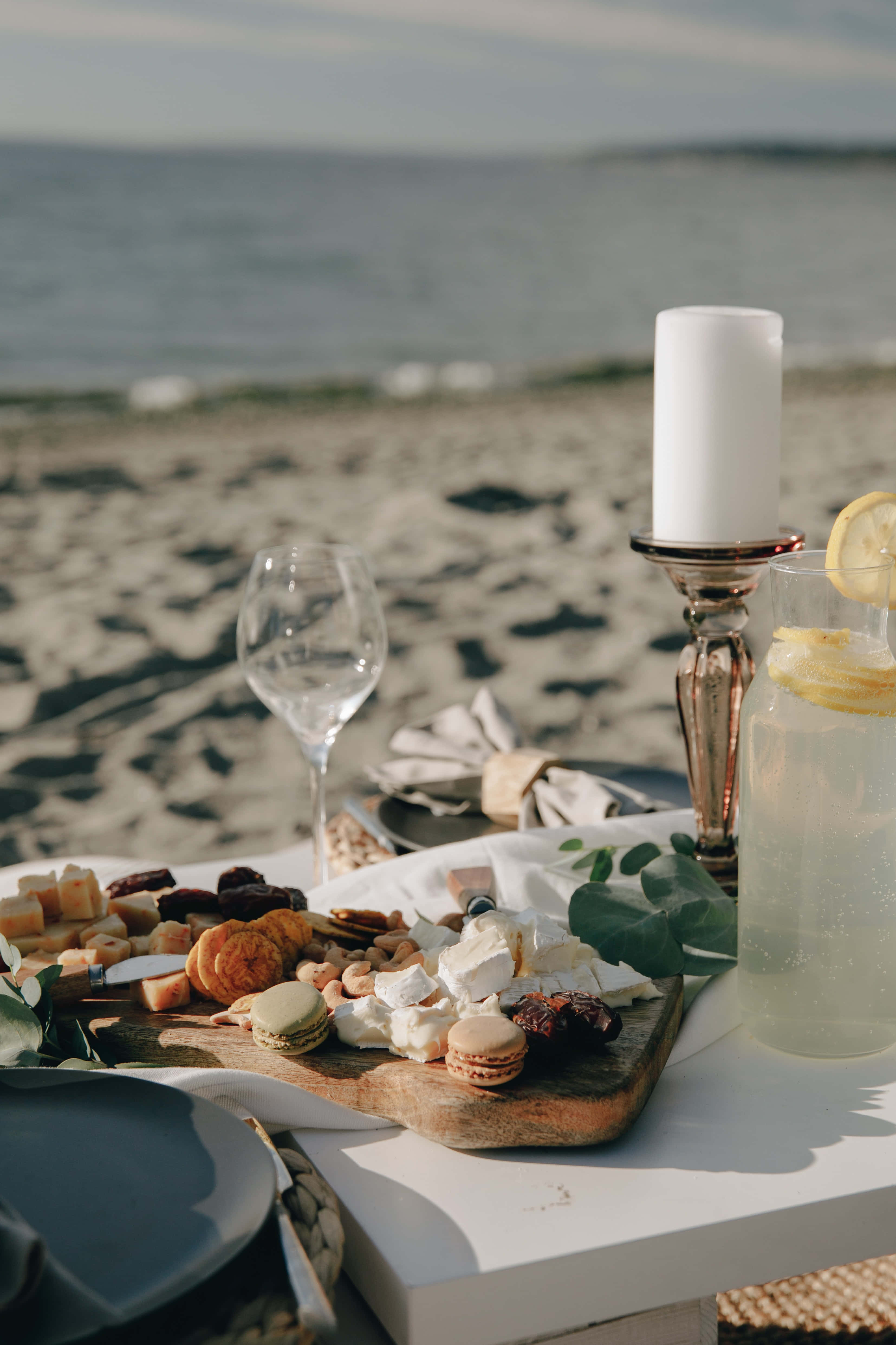 Beach Picnic 桌布 壁紙 — 海邊野餐桌擺放著芝士馬卡龍和檸檬水，在柔和日光下。