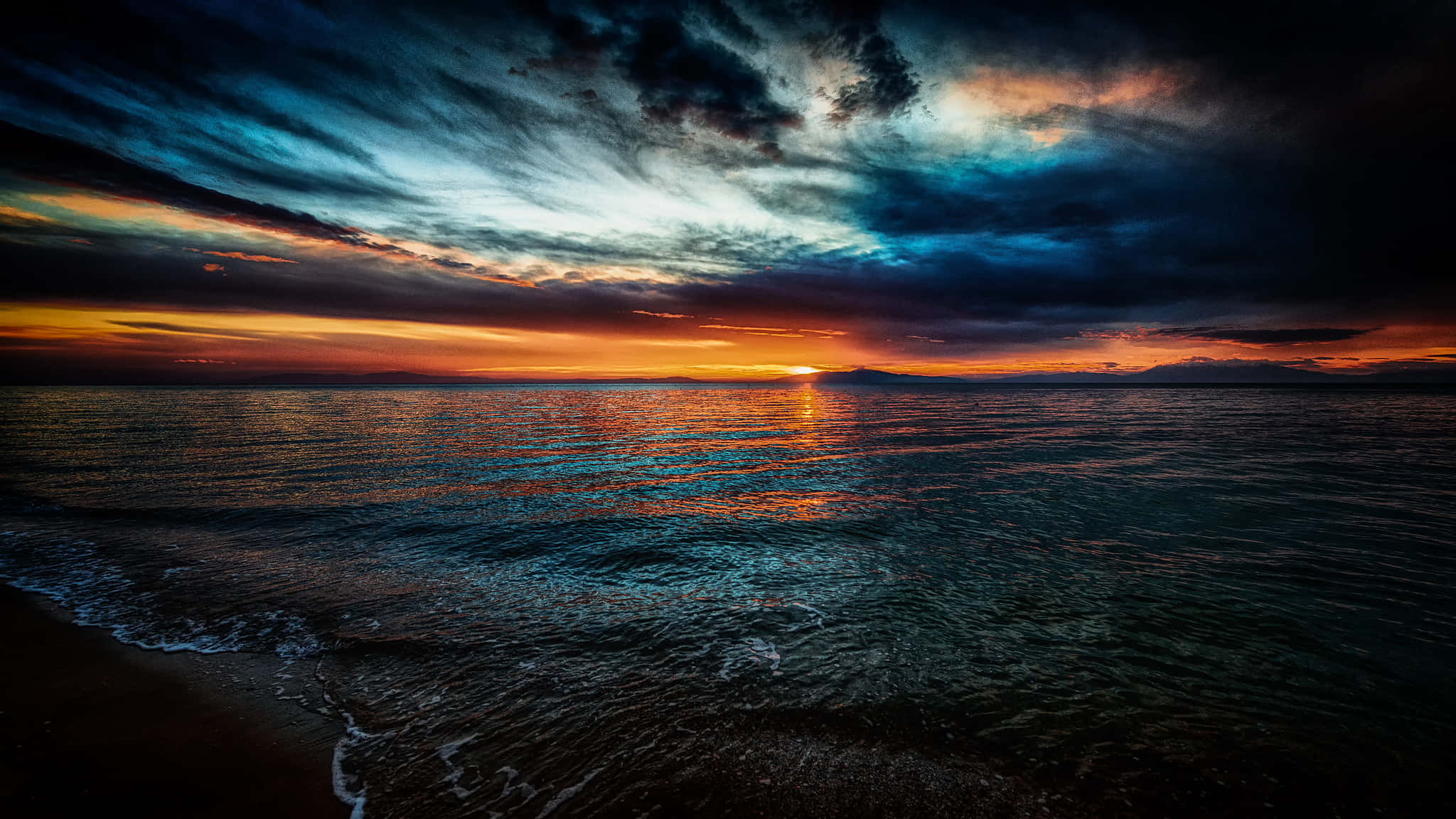 海面上的夕陽 壁紙 — 平靜海洋上戲劇性的日落，火橙色和深藍色雲彩映照在漣漪水面上。