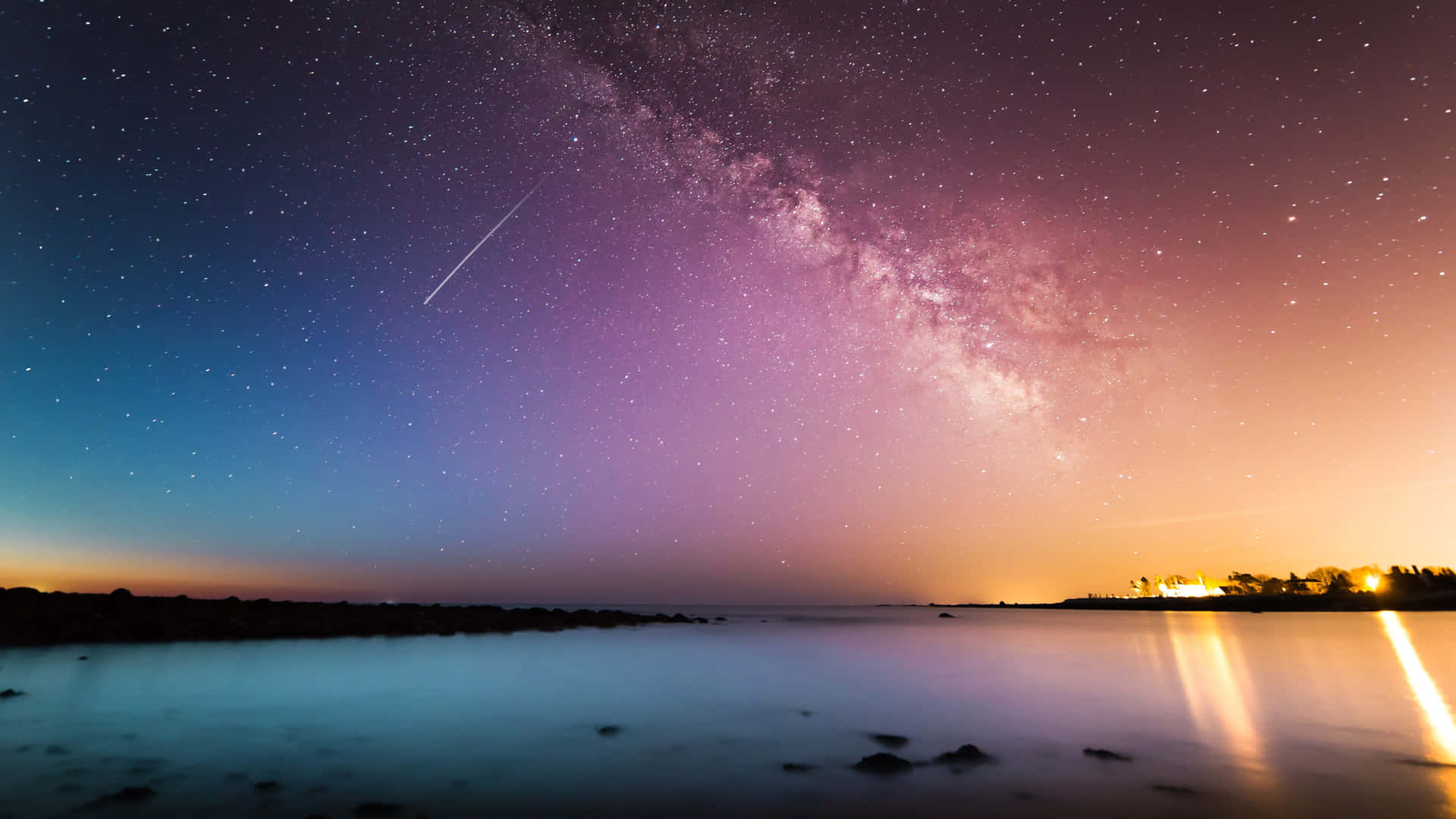 暮色中寧靜湖面上的銀河與彗星，反射著遠方的燈光。