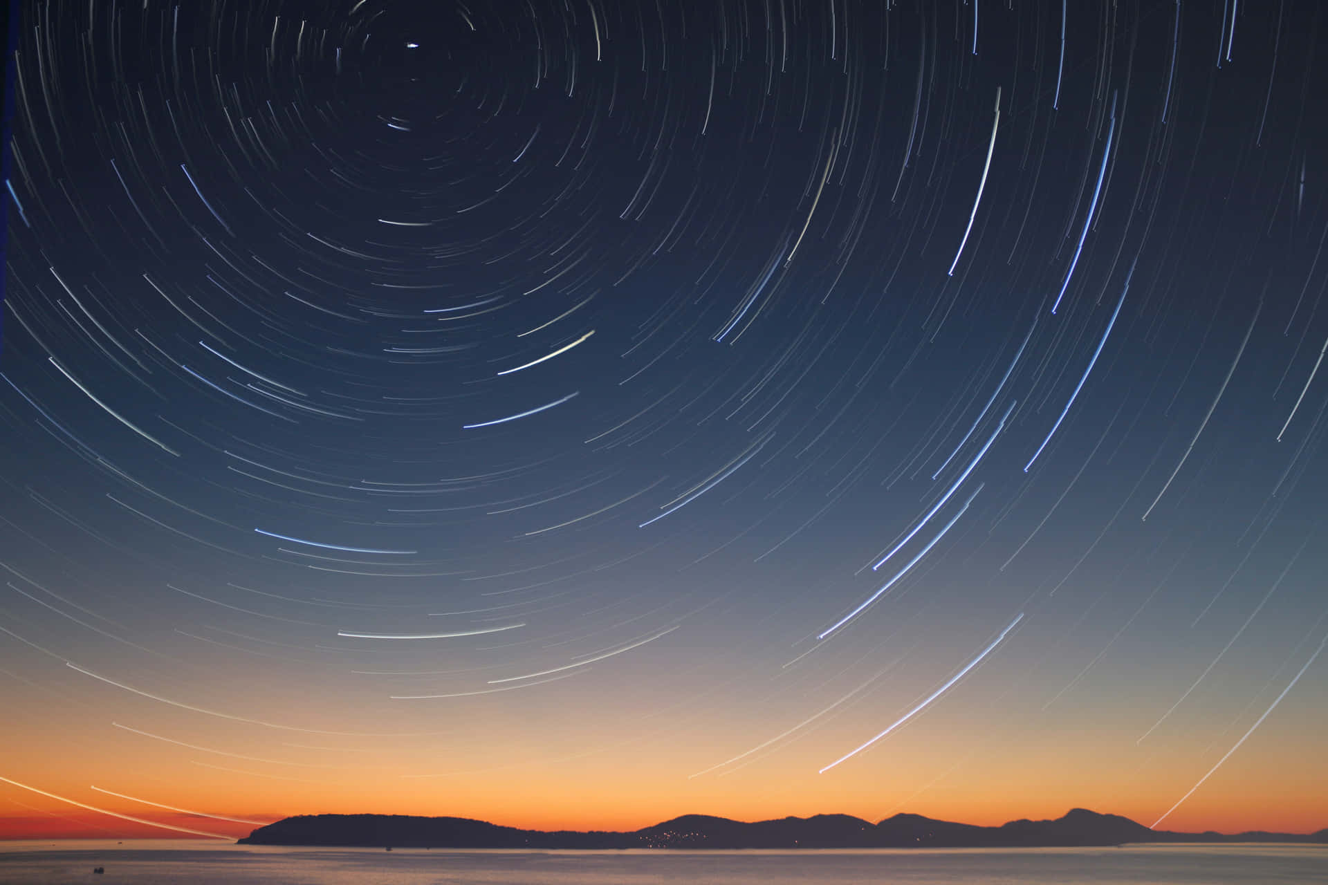 星軌在平靜的海面和山脈上空劃出弧線，時值黃昏。