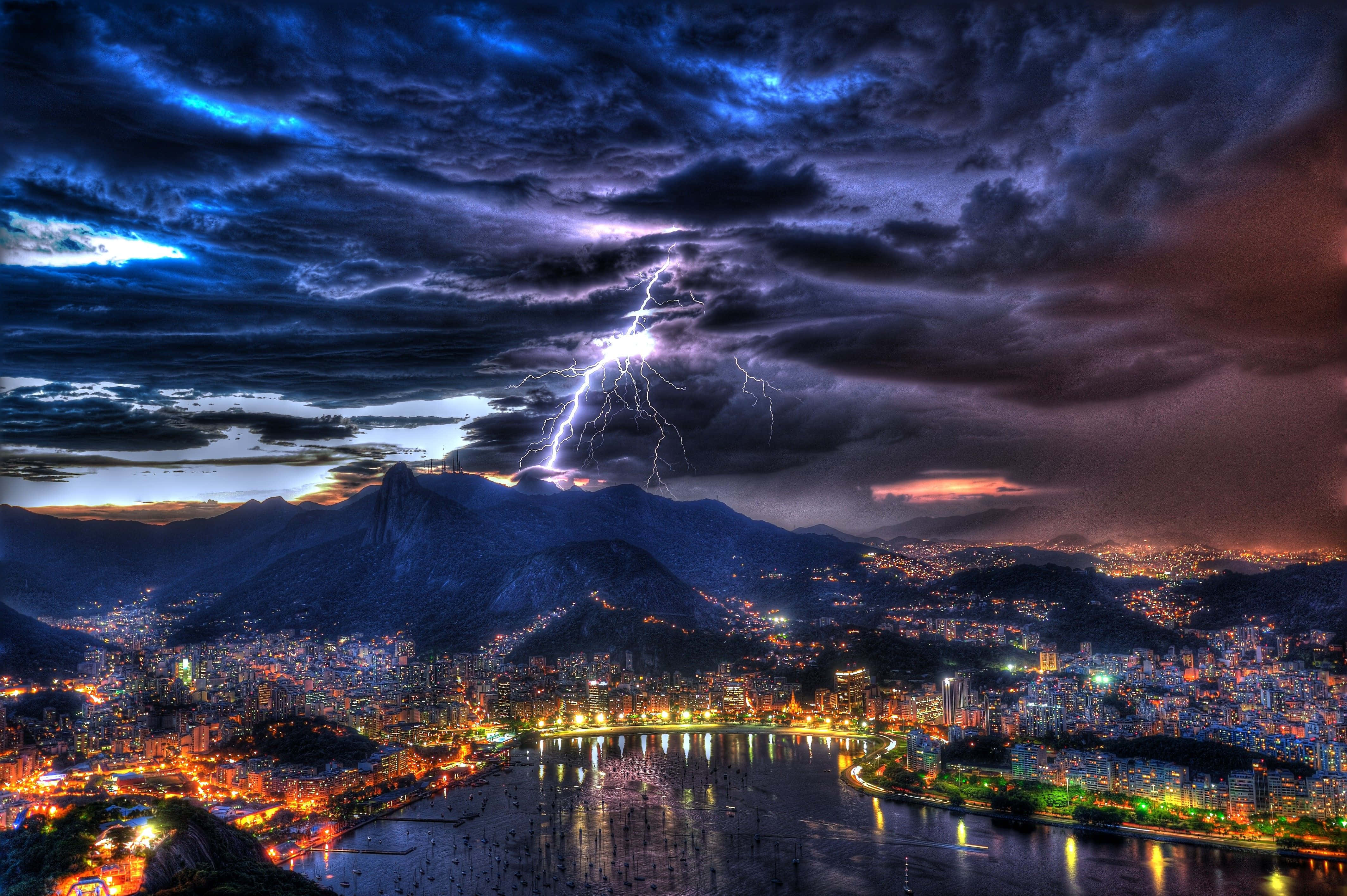 海面上的暴風雨 壁紙 — 一道戲劇性的閃電劃過黃昏時分坐落於山脈與閃耀海濱之間的廣闊城市。
