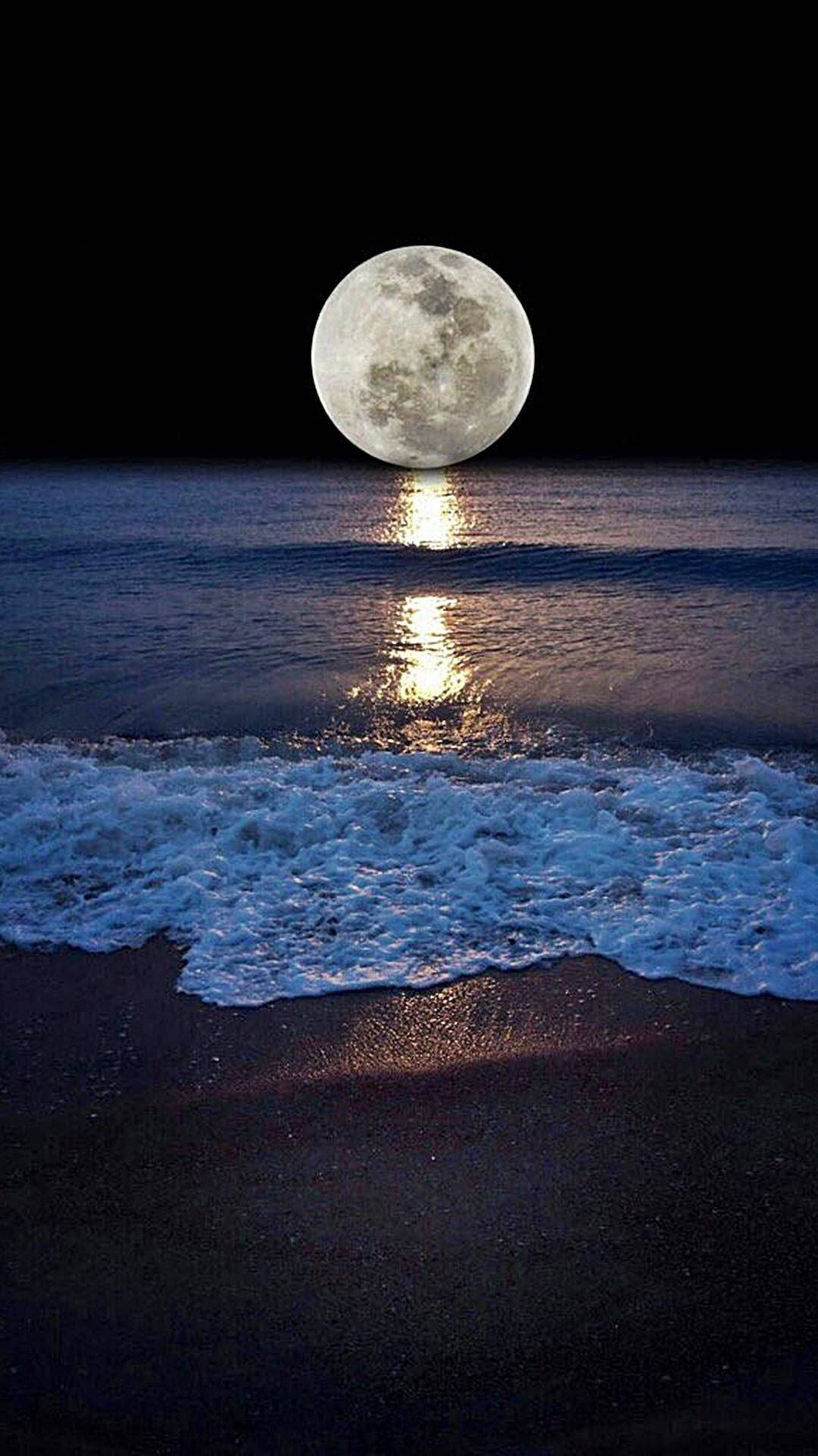 滿月映照在夜晚黑色沙灘的海浪上。