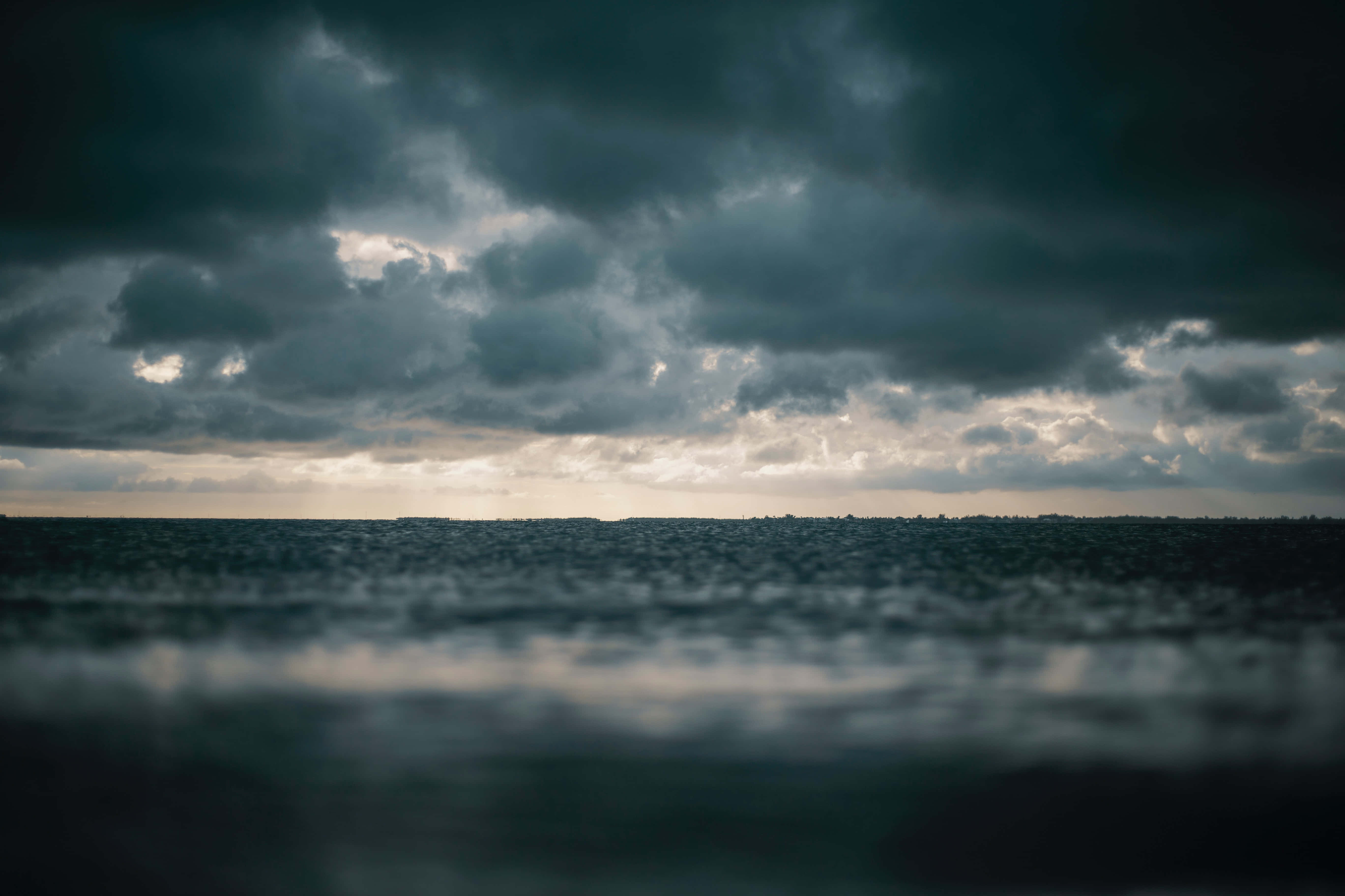 海面上的黑暗天空與背景中的船隻 壁紙 — 在厚重風暴雲下，陽光穿透地平線的陰鬱海景。