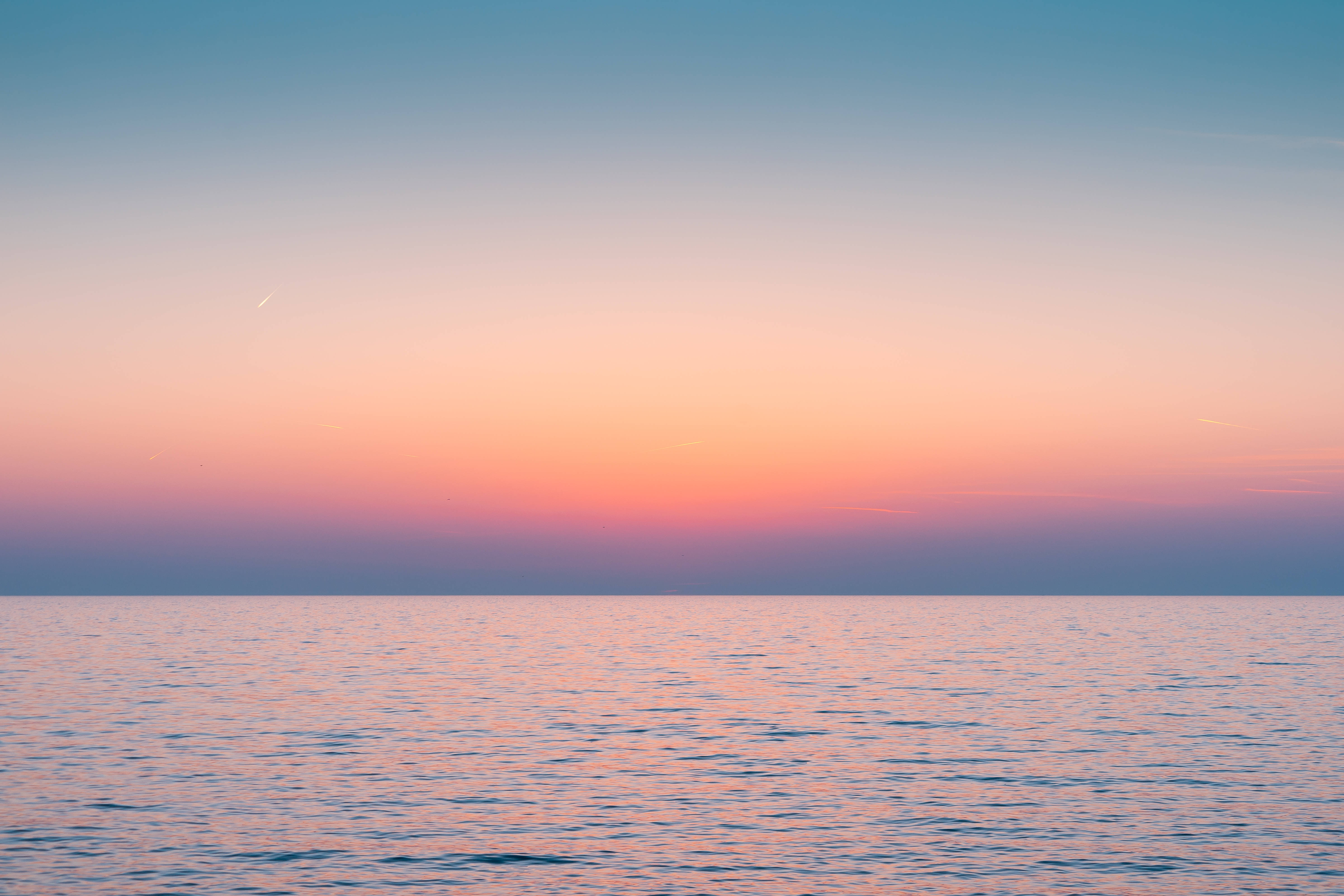 海面之上紫橙藍色天空美學壁紙 壁紙 — 晴朗天空下，平靜海洋在日落時分映照出柔和粉紅、橙和藍色調。
