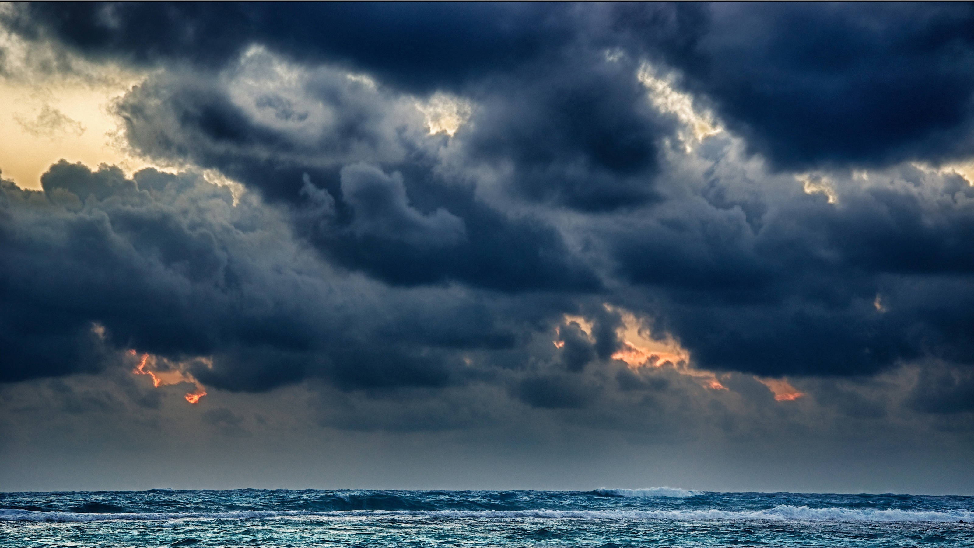 海面的烏雲暴風 壁紙 — 戲劇性的暴風雲籠罩著波濤洶湧的海洋，金色的光芒穿透黑暗的天空。