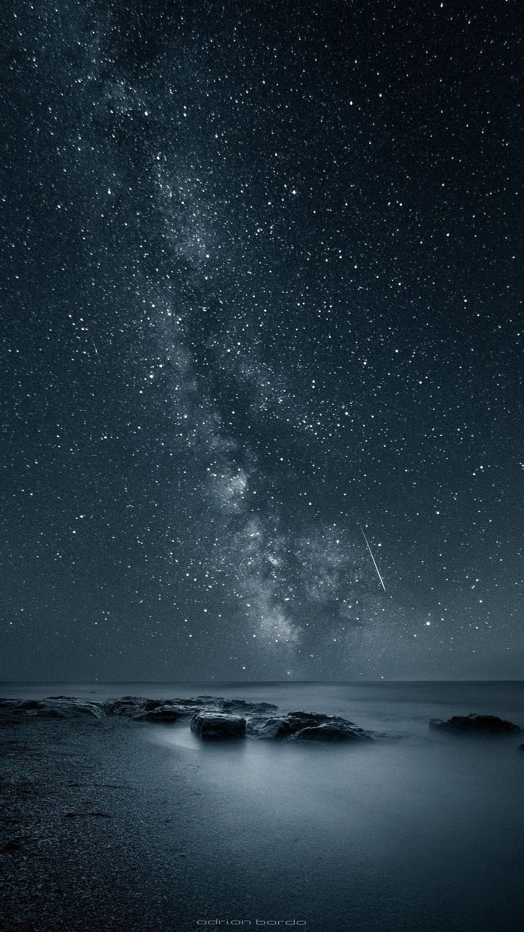 在繁星點點的夜空下，銀河系位於黑暗的海洋岩石之上