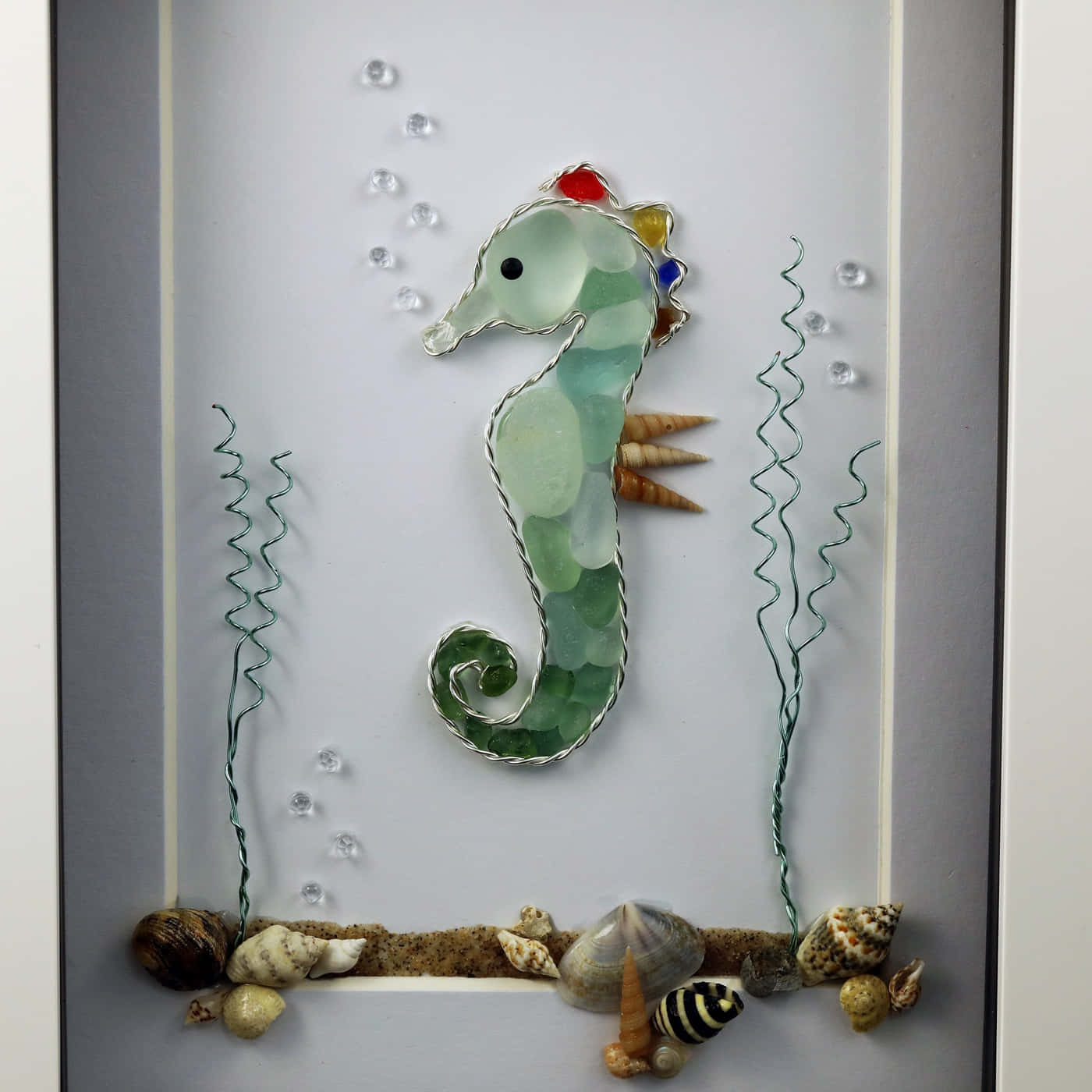 海馬海玻璃圖 壁紙 — 一個用綠色海玻璃和金屬線製成的海馬立體藝術品，鑲在畫框內，周圍有貝殼和氣泡。
