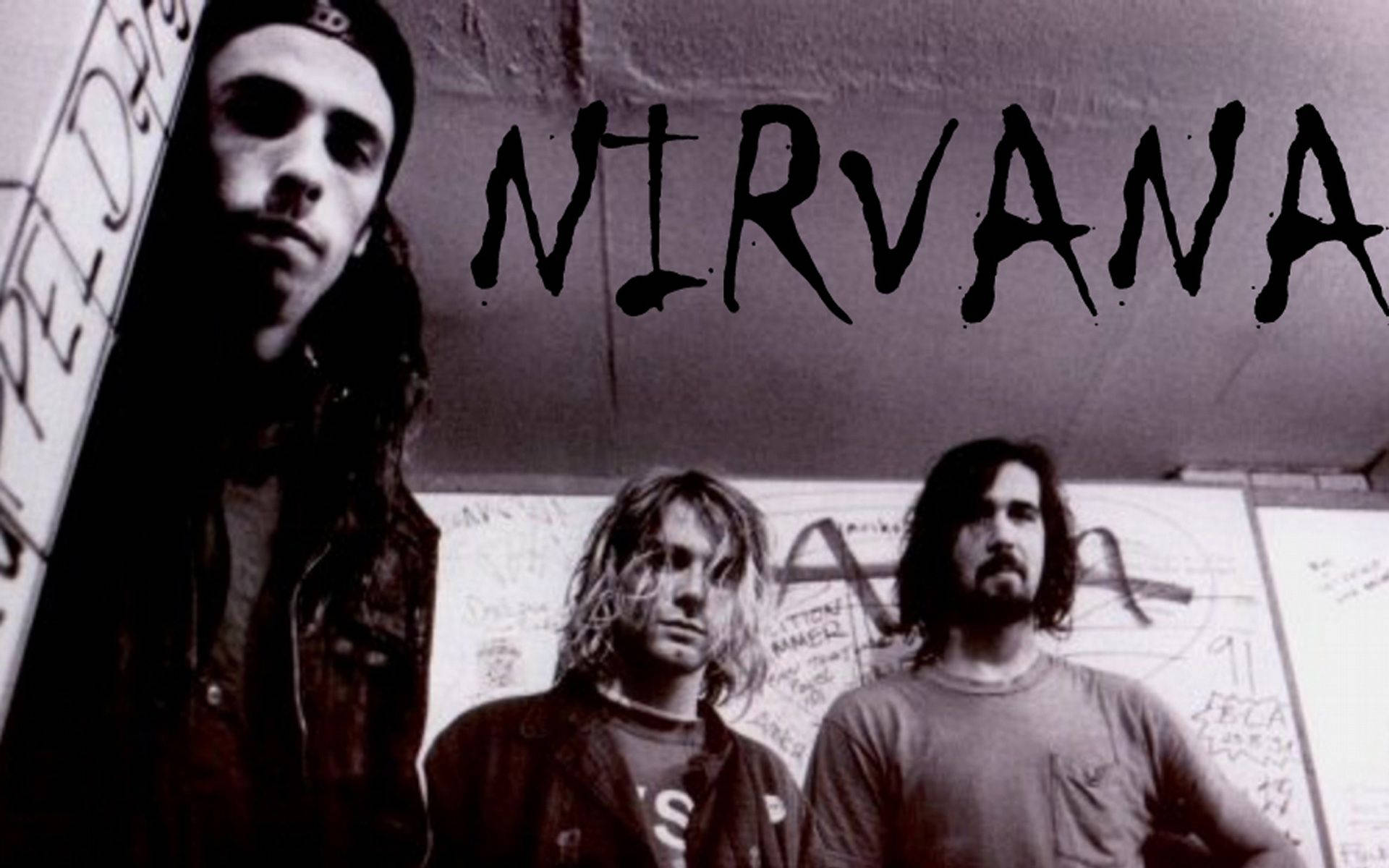 三名垃圾搖滾風格男子在帶有「NIRVANA」文字的塗鴉牆前擺姿勢。