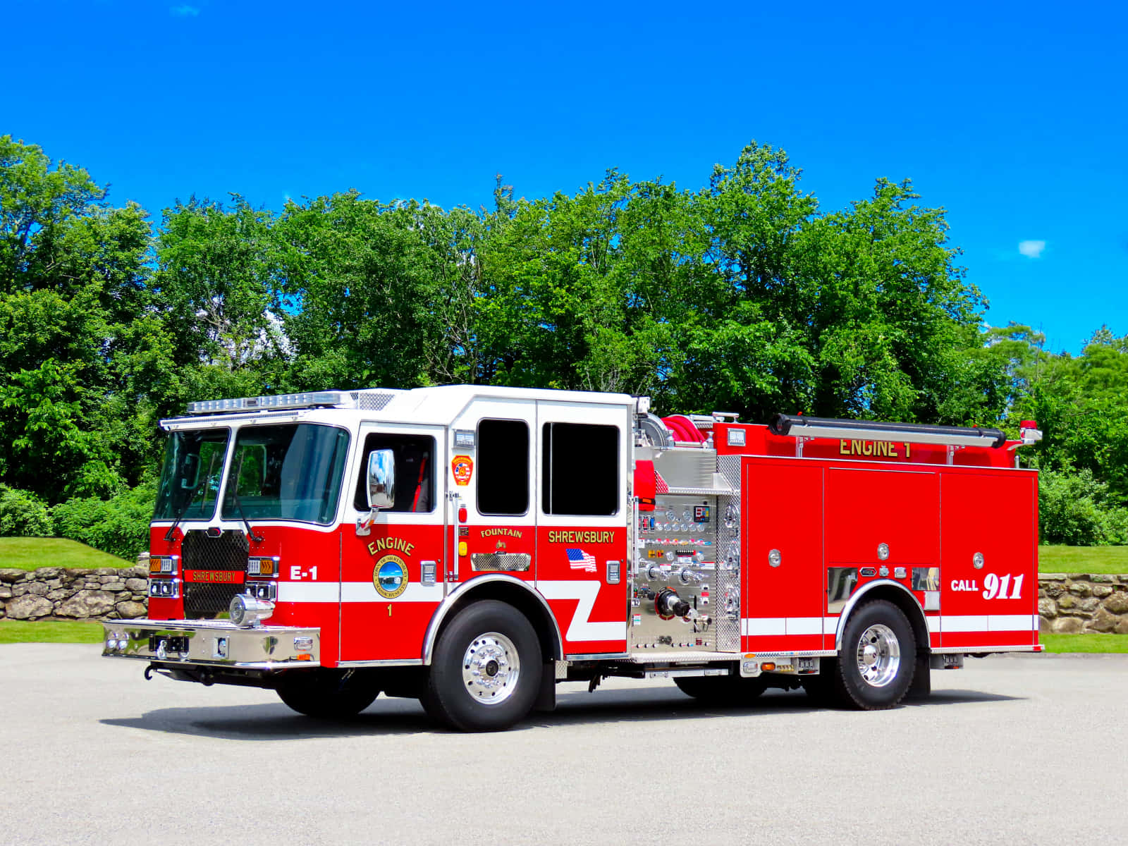 消防員應對緊急求助 壁紙 — 一輛鮮紅色的Shrewsbury Engine 1消防車停在瀝青路上，天空清澈湛藍，背後是茂密的綠樹。
