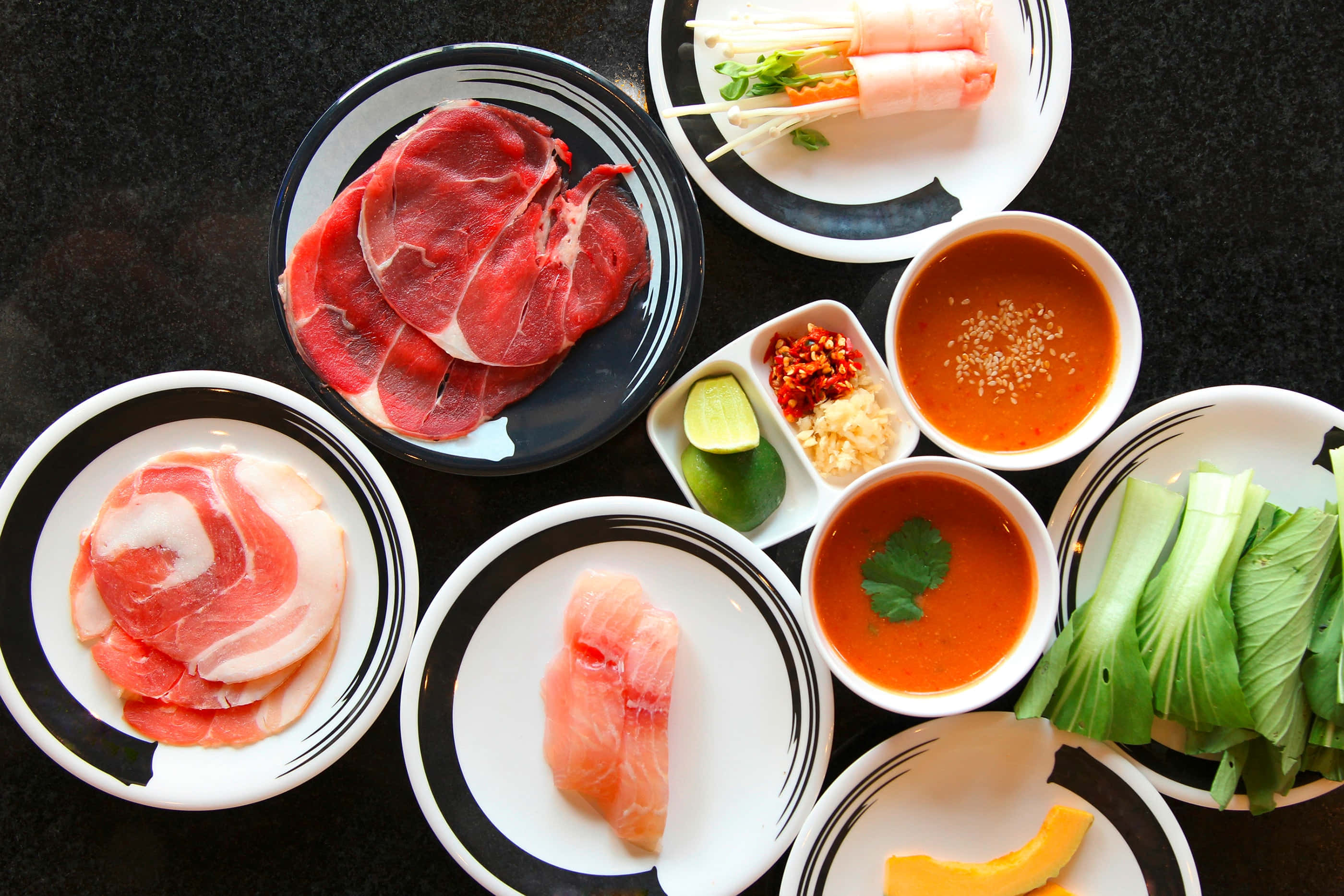 涮涮鍋食材擺盤 壁紙 — 從上方俯瞰各種生肉、魚類和新鮮蔬菜整齊排列在黑白色碟子上，準備烹調。