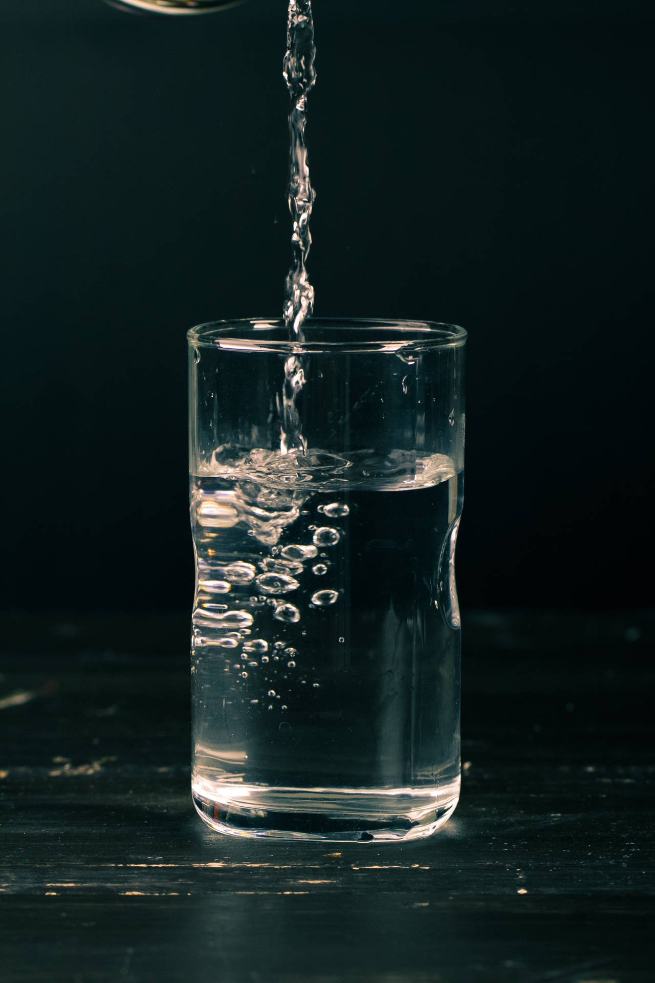 水倒入玻璃杯中，在深色表面上形成氣泡。
