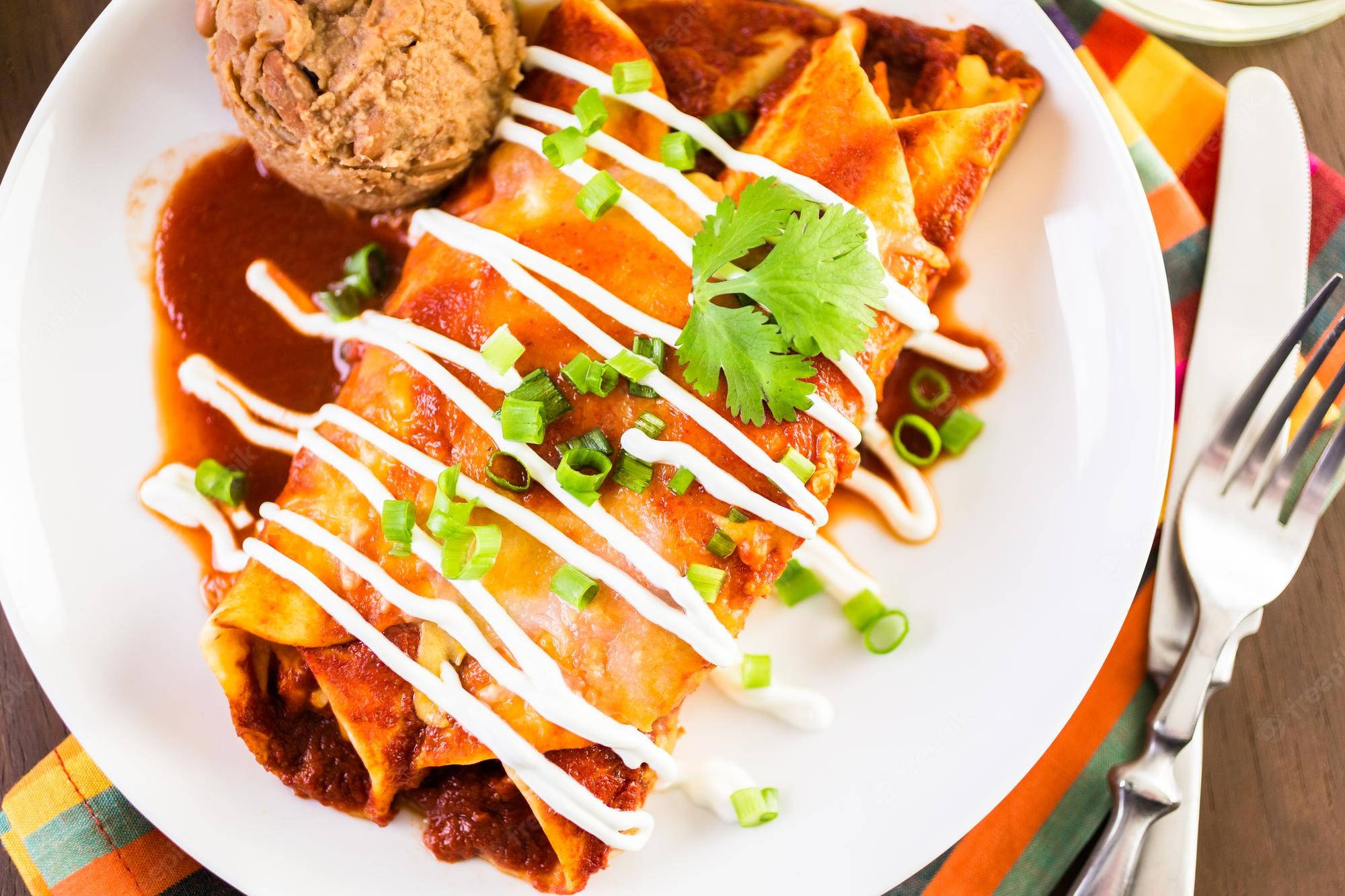 淋上蛋黃醬的 enchiladas 壁紙 — 金黃色辣醬玉米餅，浸在紅醬中，淋上奶油，並以新鮮芫荽和青蔥點綴。