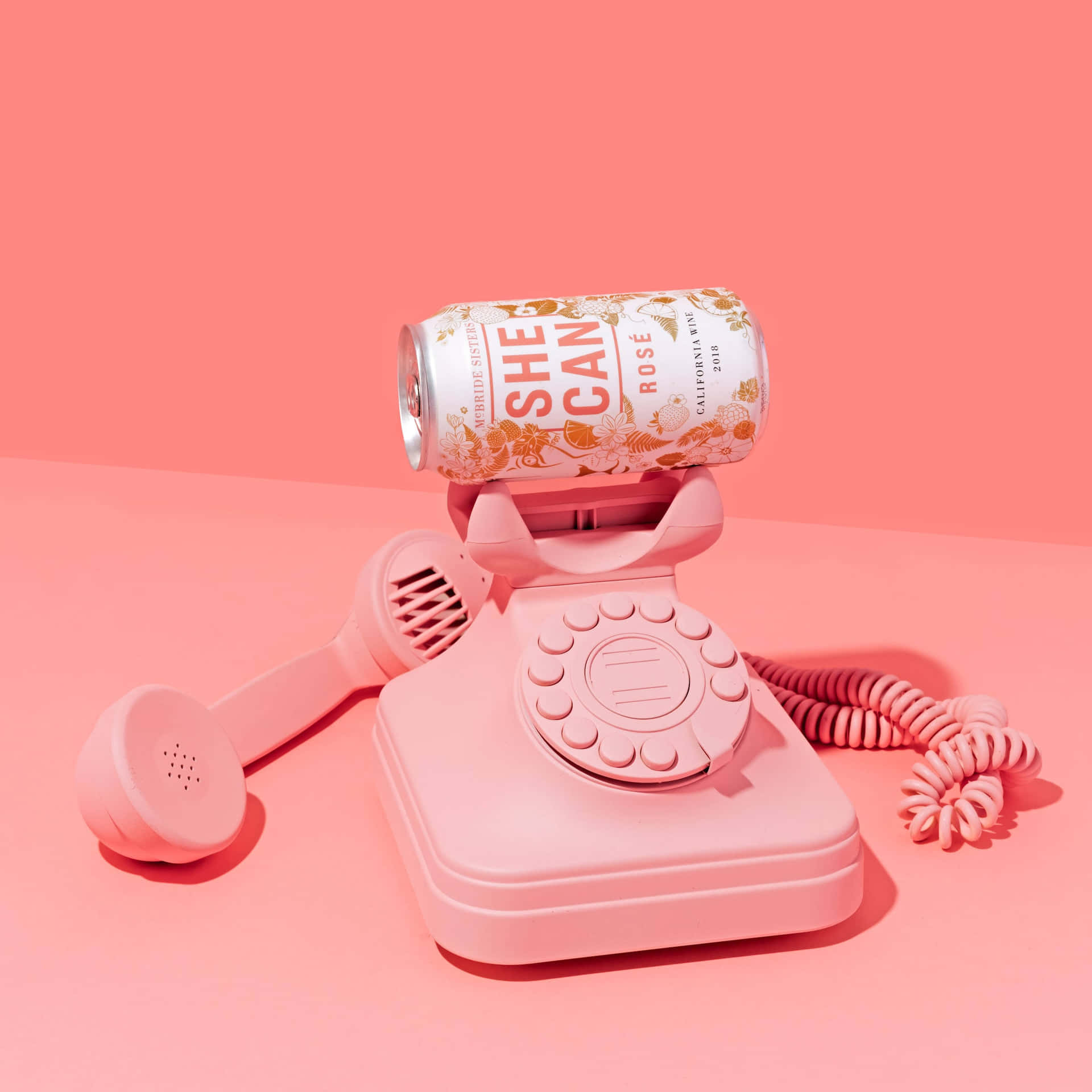粉紅色轉盤電話機拿著一個標籤為 She Can Rosé 的粉紅色葡萄酒罐。