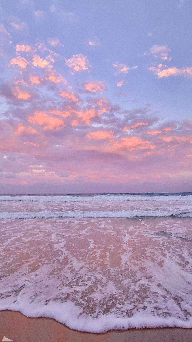 粉紅色和紫色的日落映照在海浪和沙灘上