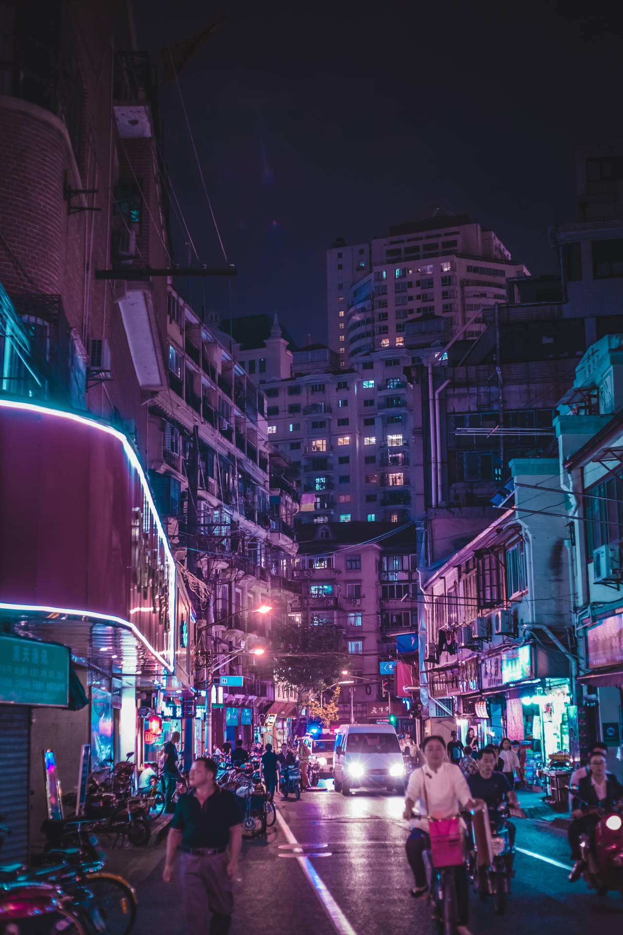 夜晚的城市街道，有霓虹燈招牌和騎單車的人。
