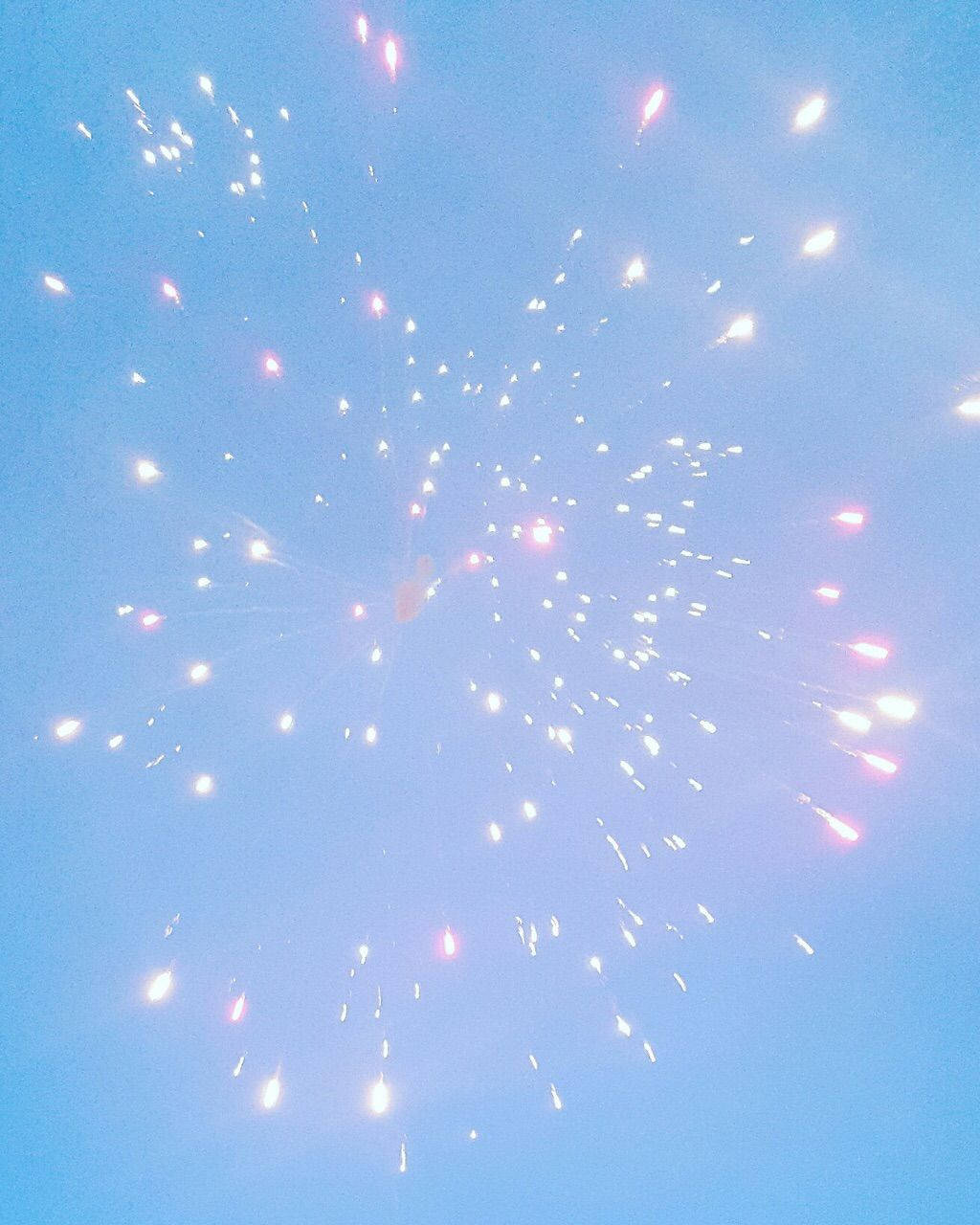 煙花在清澈的藍天中爆炸，帶有柔和的粉紅色和白色火花。