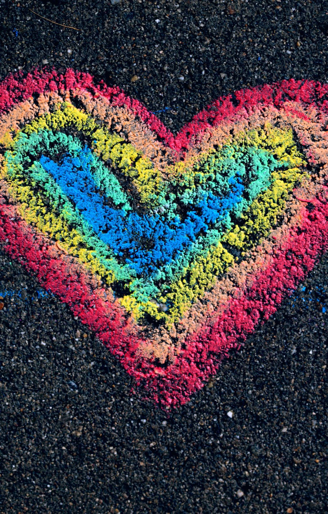 淡雅 LGBT 雨虹心形粉筆藝術 壁紙 — 在深色瀝青上用粉筆繪製的充滿活力的彩虹心，展現出紋理豐富、色彩繽紛且俏皮的街頭藝術作品。