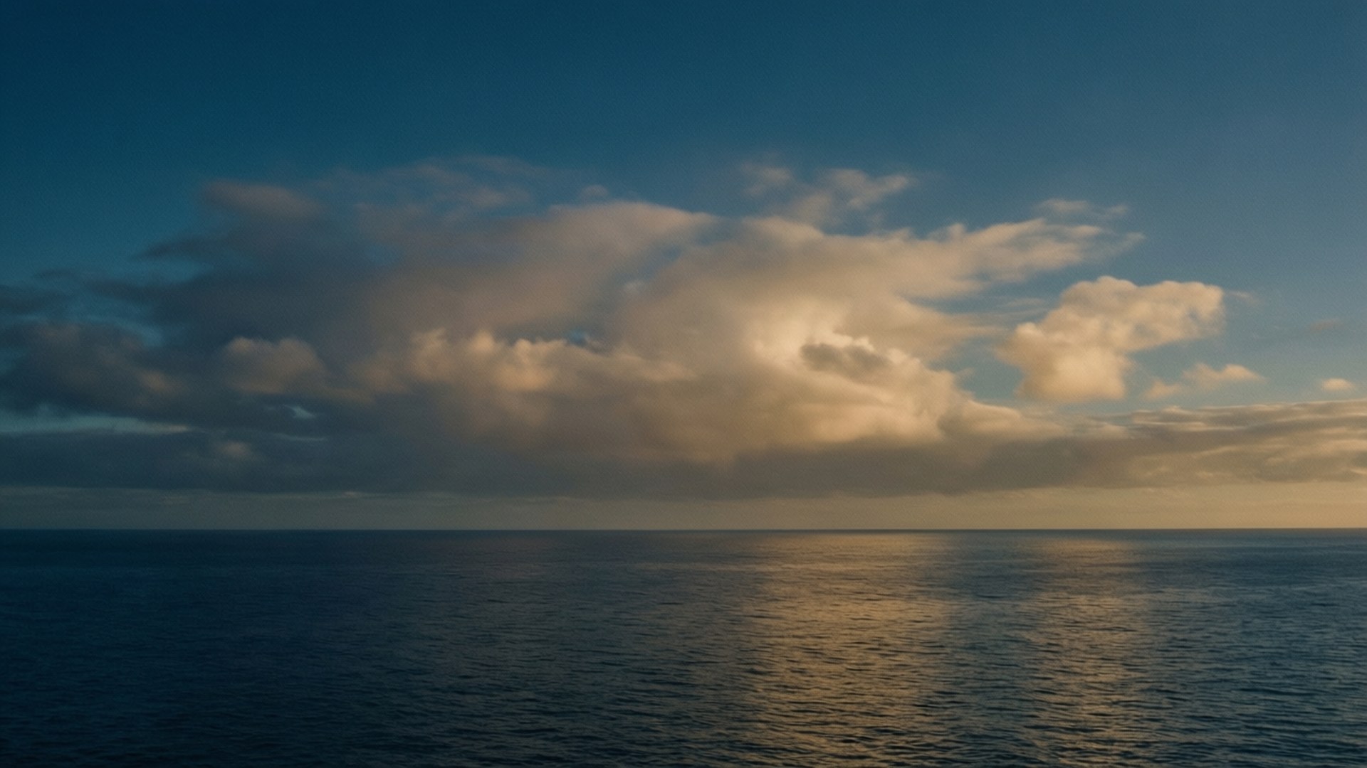 海洋上的日落，金色雲彩倒映在平靜的水面上。