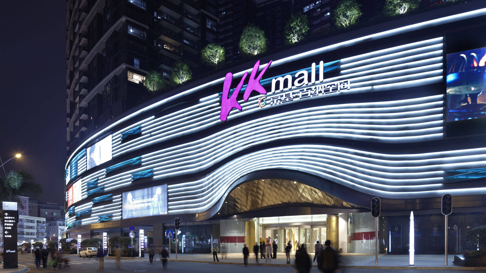 深圳KK Mall 壁紙 — 未來感購物中心夜景，白色與紫色霓虹燈沿著現代化外牆彎曲閃耀。