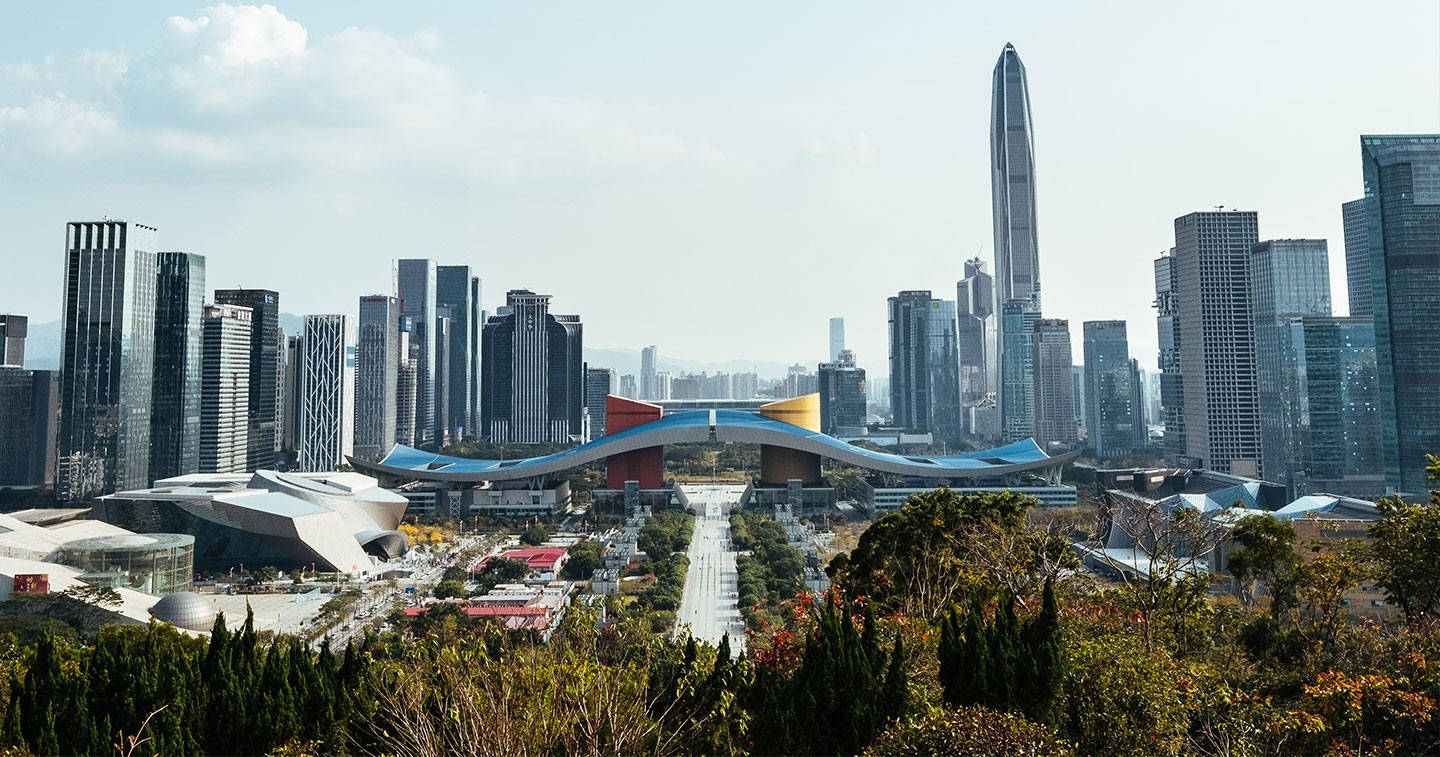 深圳市民中心 壁紙 — 現代城市天際線的全景視圖，玻璃摩天大樓和色彩繽紛的未來主義橋樑在部分多雲的天空下。